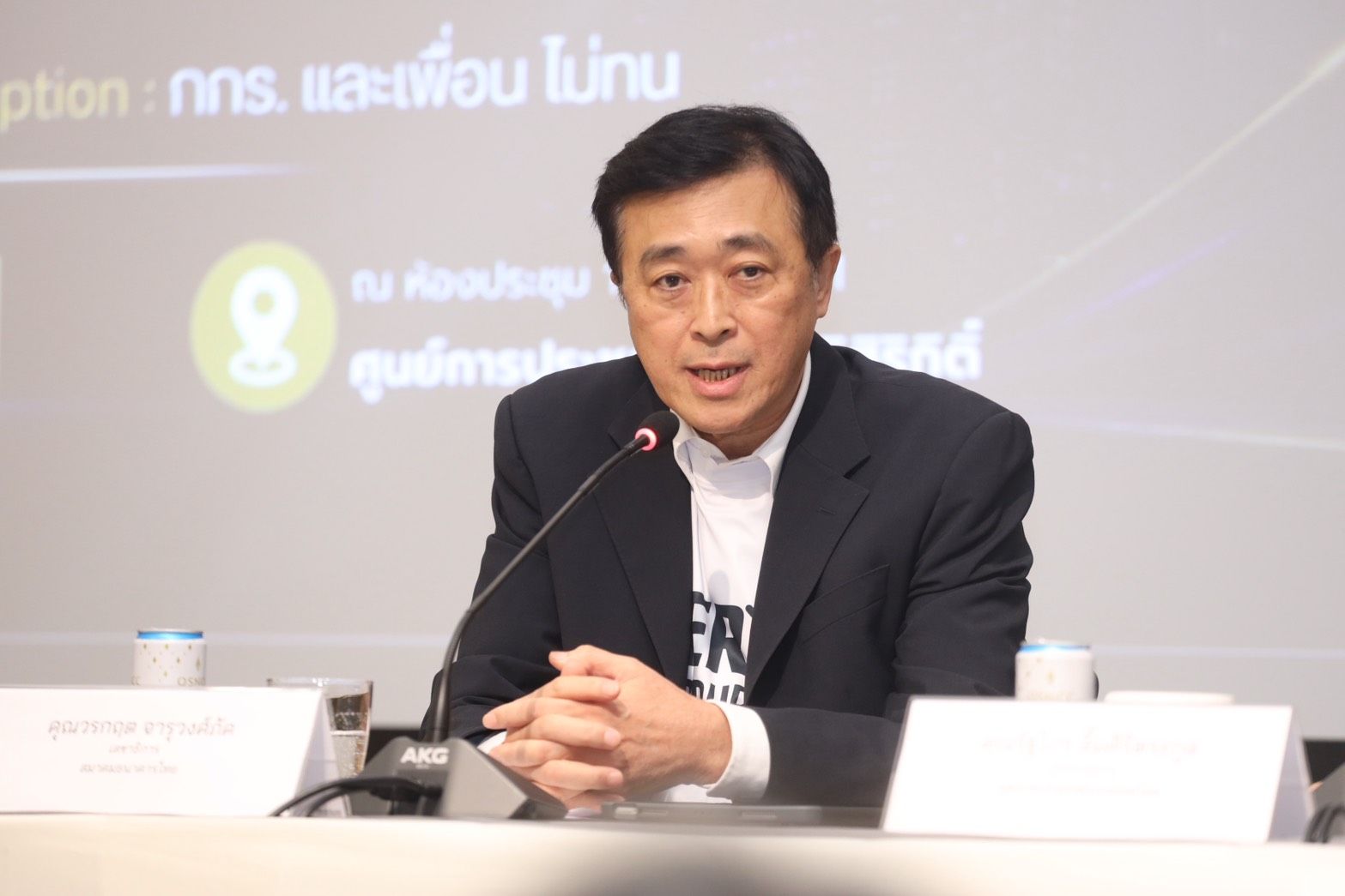 East Asian man in a suit speaks at a podium with hands clasped.