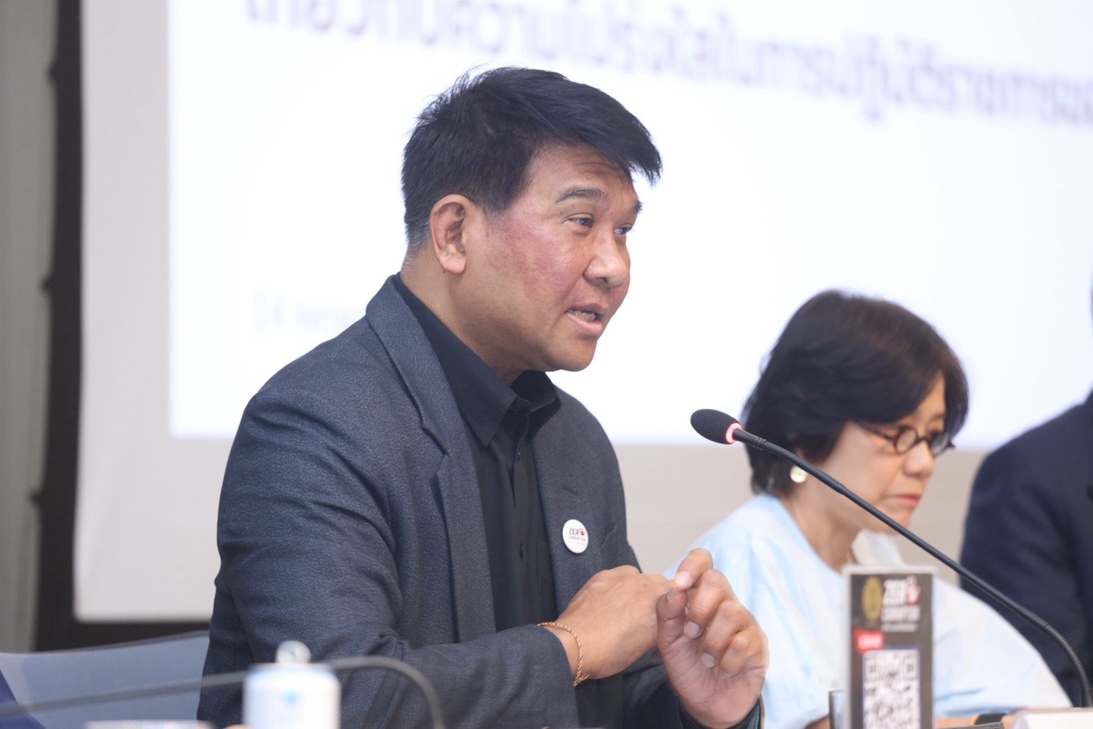Man in a black jacket speaking intently into a microphone at a conference.