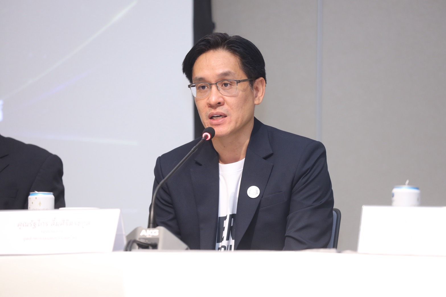 Man with glasses speaks into a microphone at a professional event or conference.