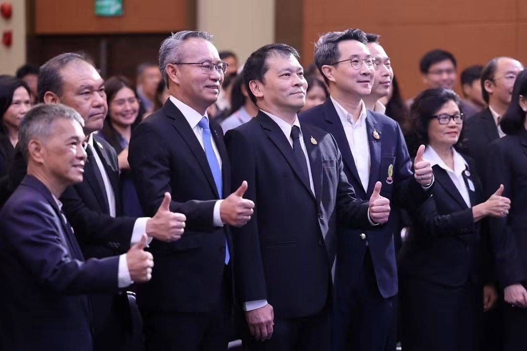 Several Asian men in suits give thumbs up gestures at an indoor event.