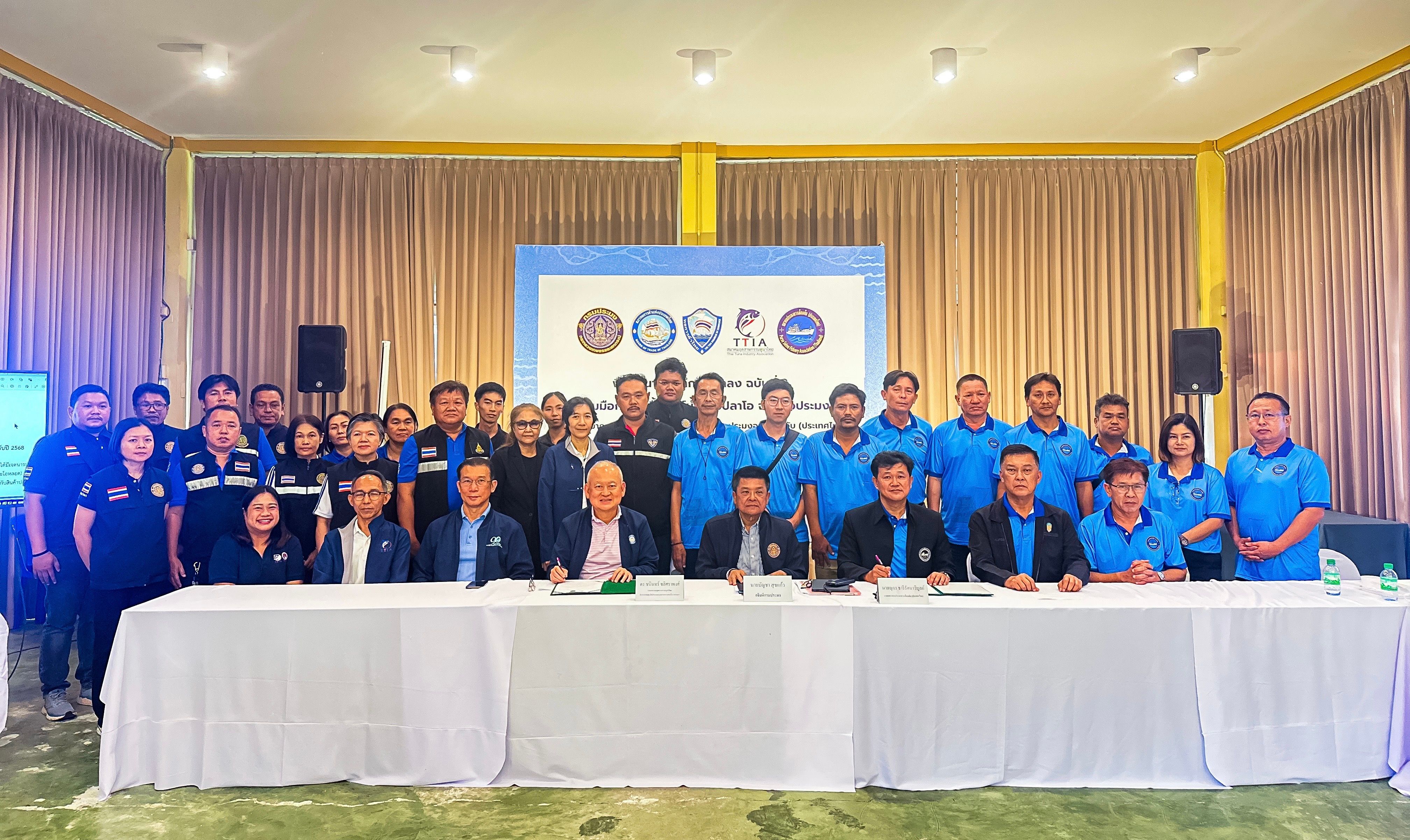A large group of people in blue shirts pose for a photo in a meeting room.