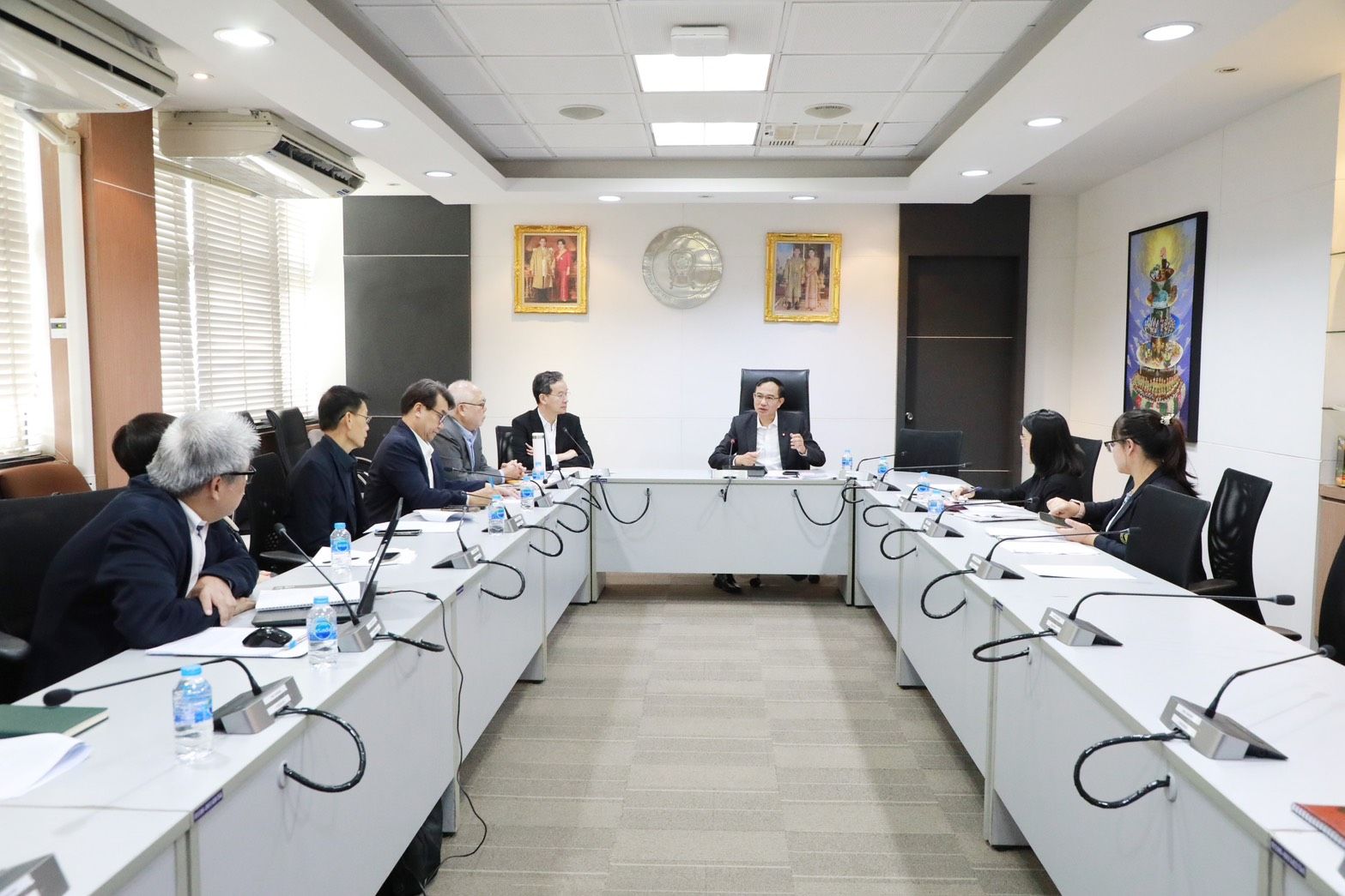 Professionals seated around a U-shaped conference table in a formal meeting room.