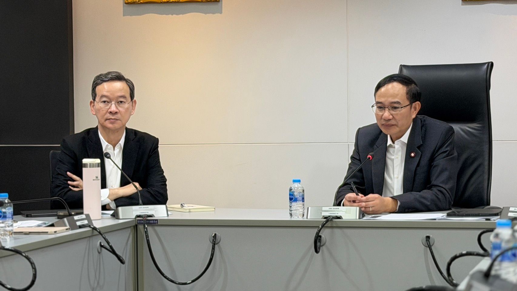 Two professional men in suits sit at a conference table during a meeting.