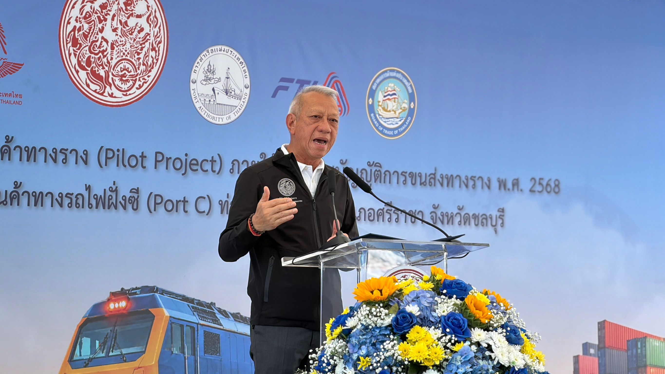Man speaking at a podium with a train and project logos in the background.