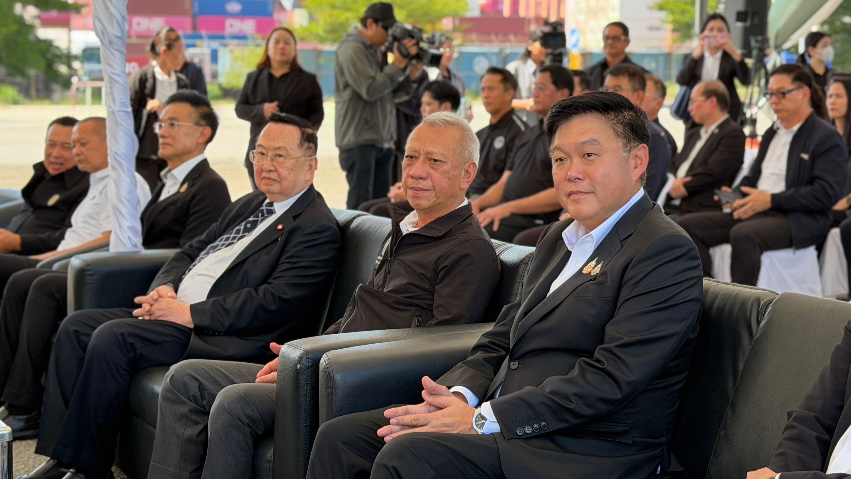 A group of formally dressed men are seated outdoors at an official event.
