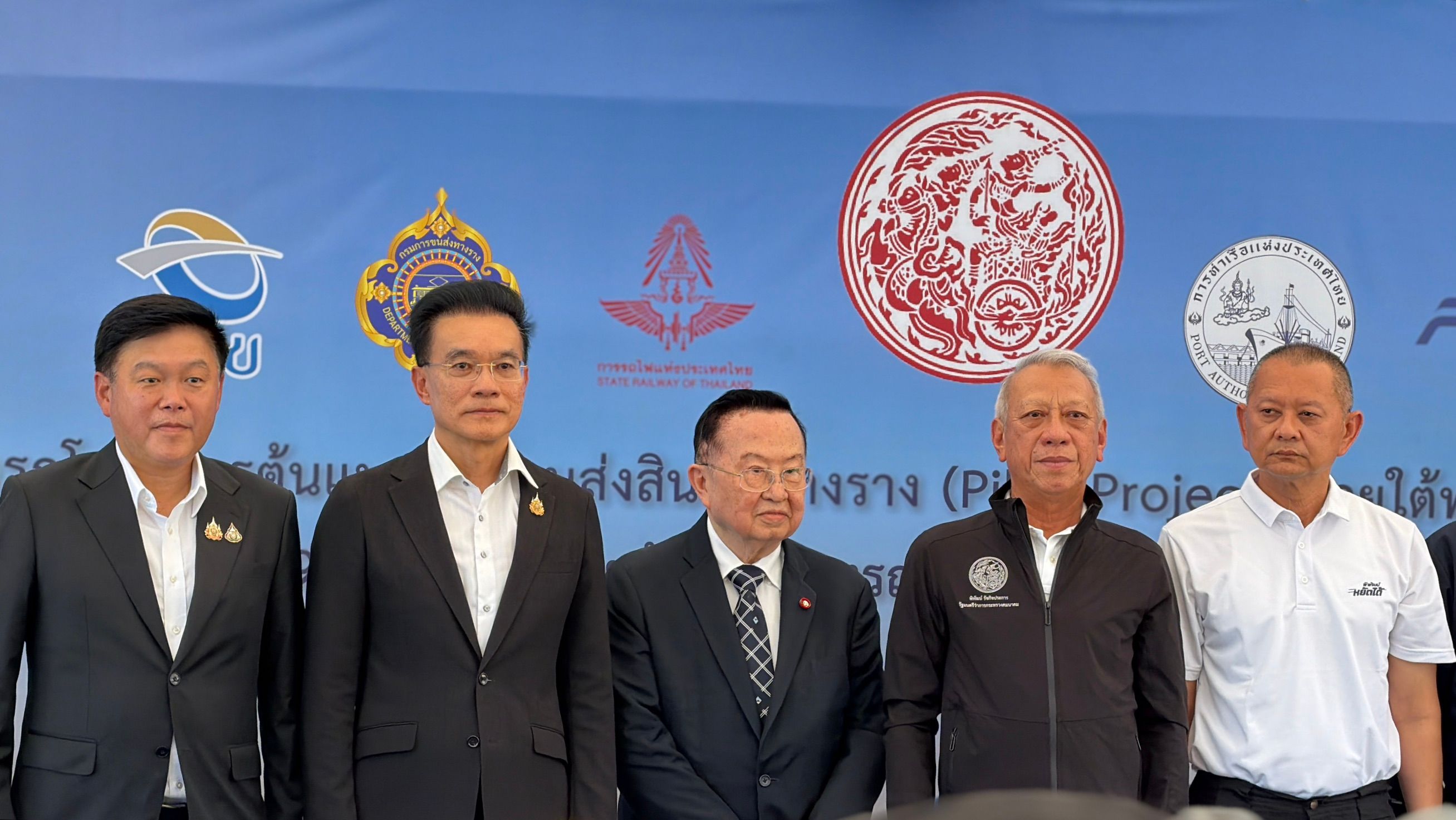 Five men in suits and collared shirts standing formally before a blue backdrop with official logos.