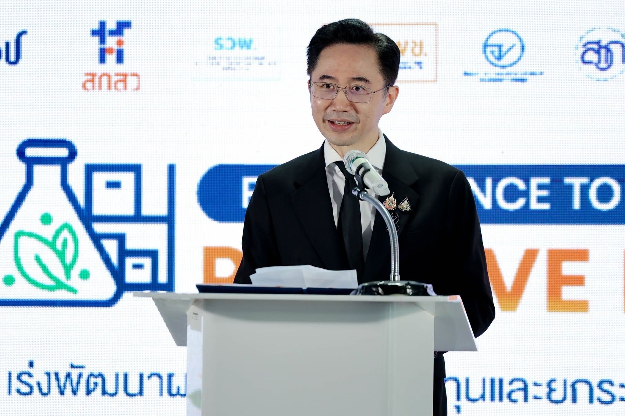 A man in a dark suit and glasses speaks at a white podium during a presentation.