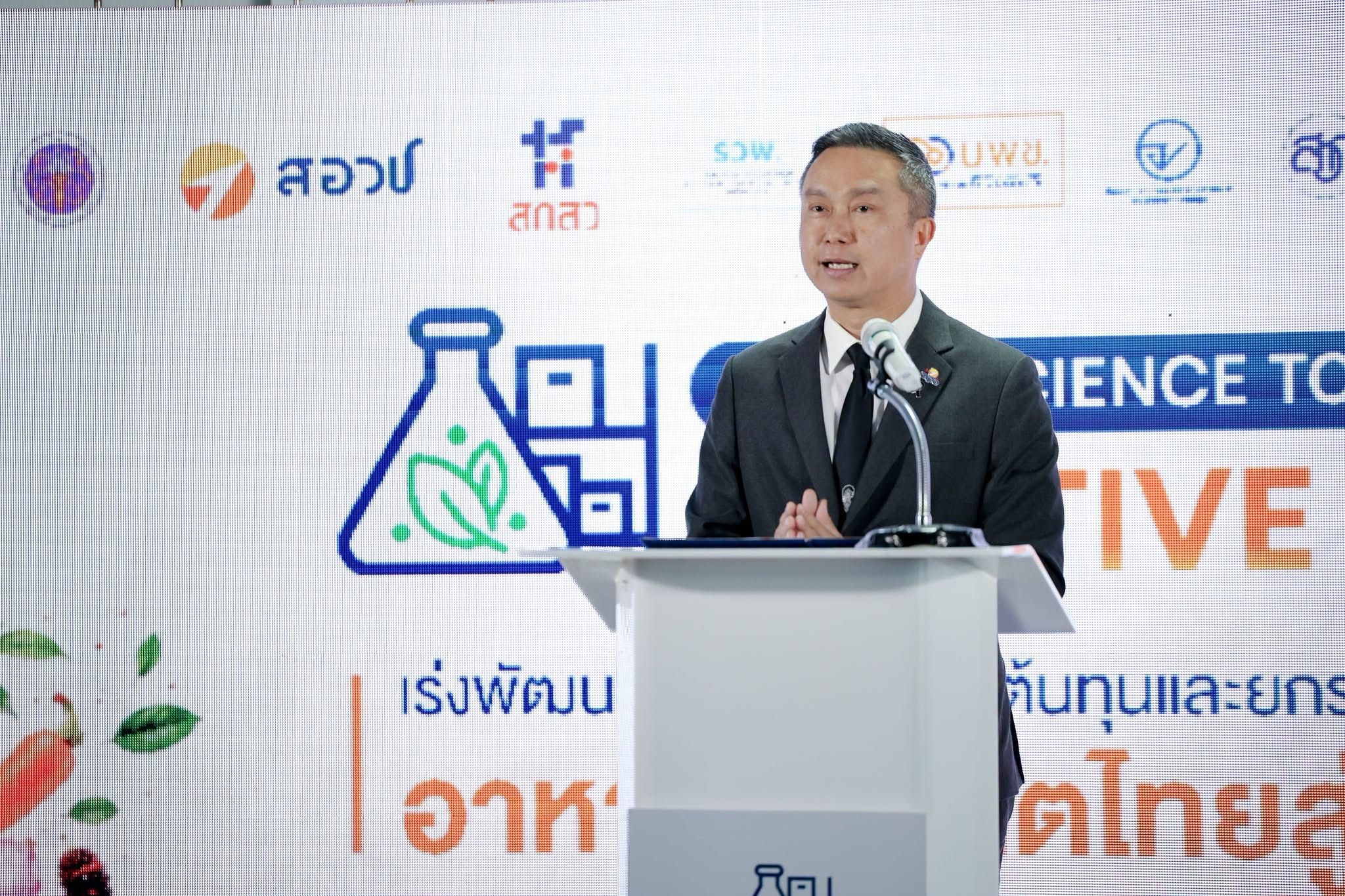 Man in suit speaks at podium before banner displaying science-related graphics and logos.