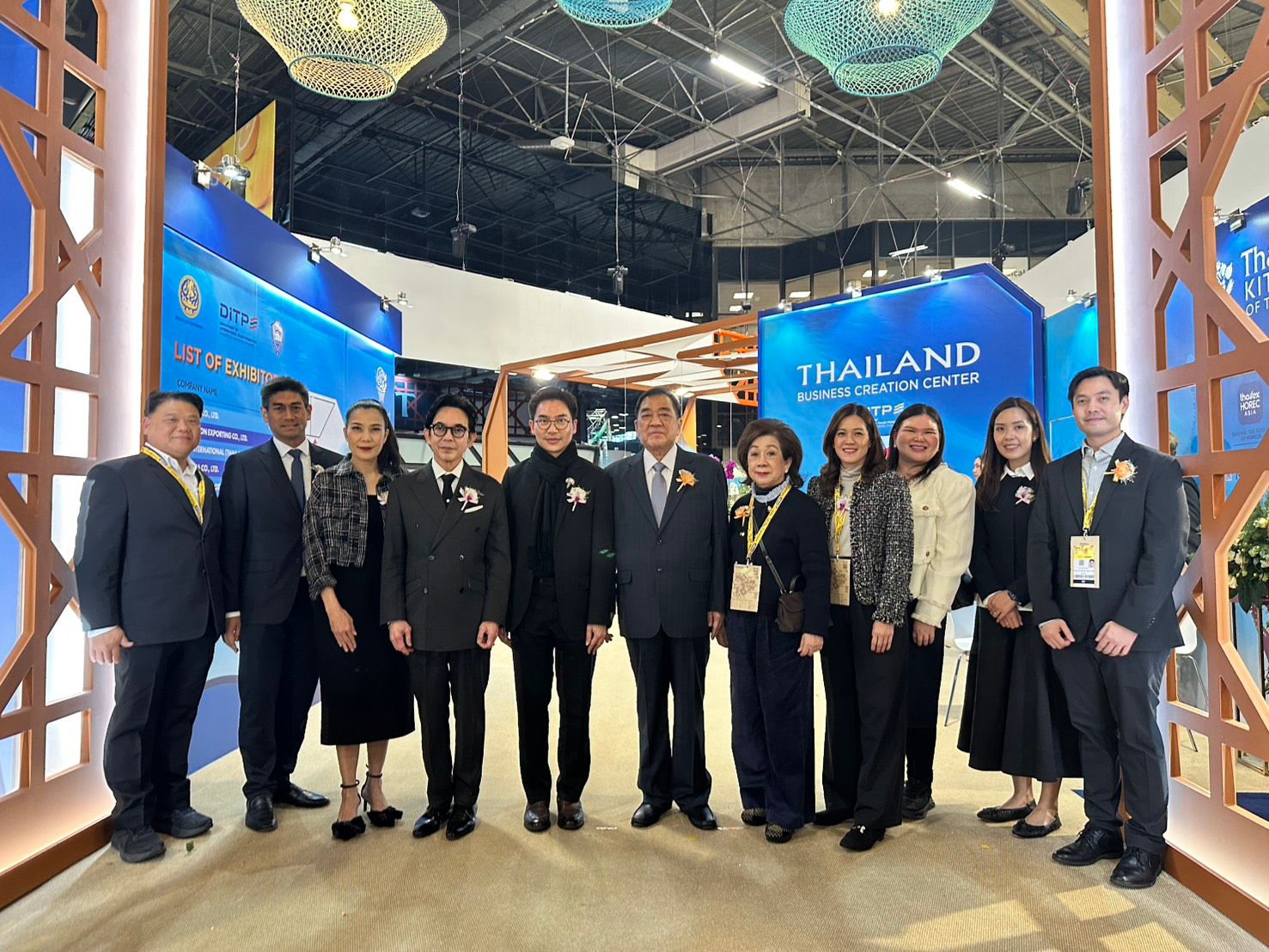 Group of delegates standing in front of a 'THAILAND' display at an exhibition.