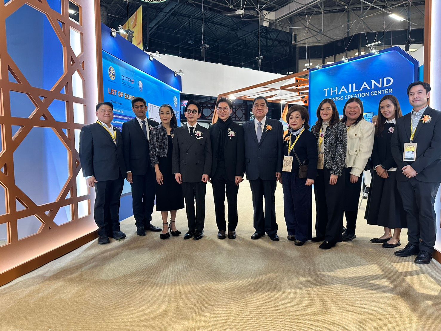 A group of formally dressed individuals stands in front of a 'THAILAND' exhibition booth.