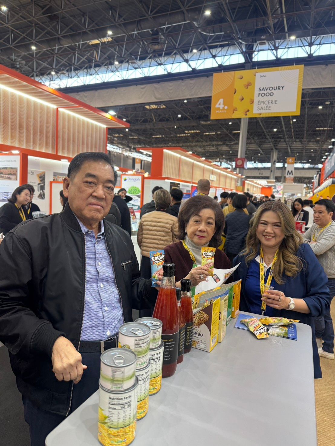 Three people smiling at a trade show booth with canned food products on display.