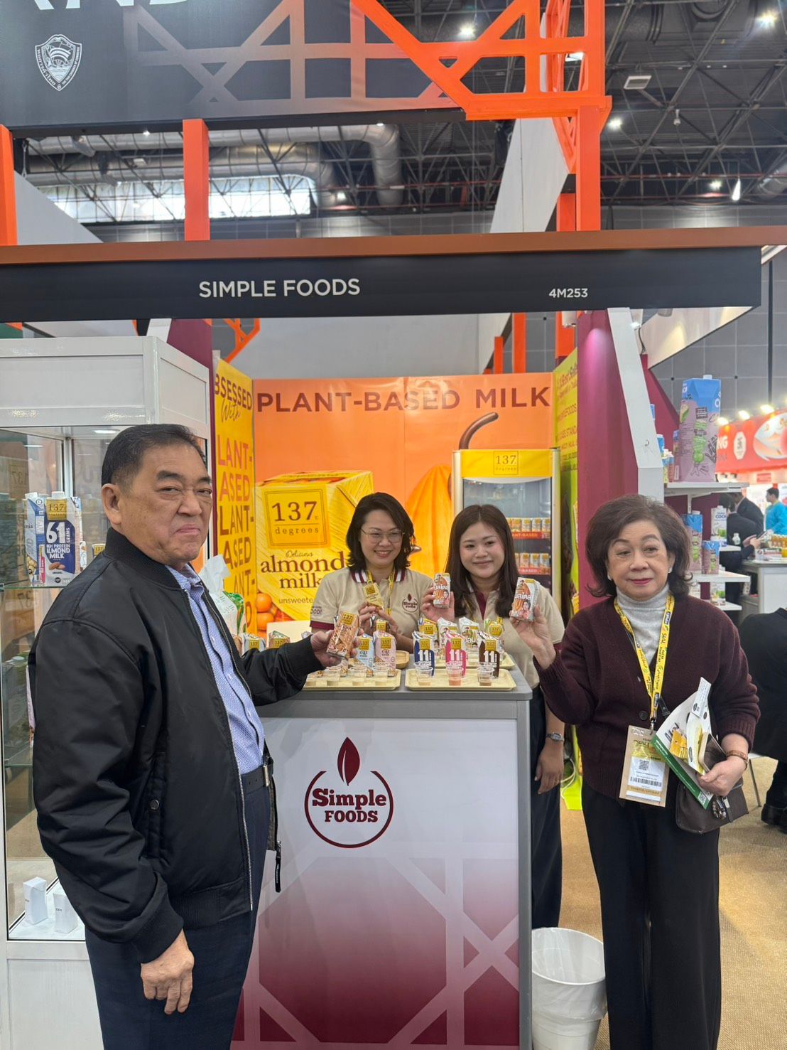 Four individuals pose at a food exhibition booth for Plum Asia Milk, displaying products.