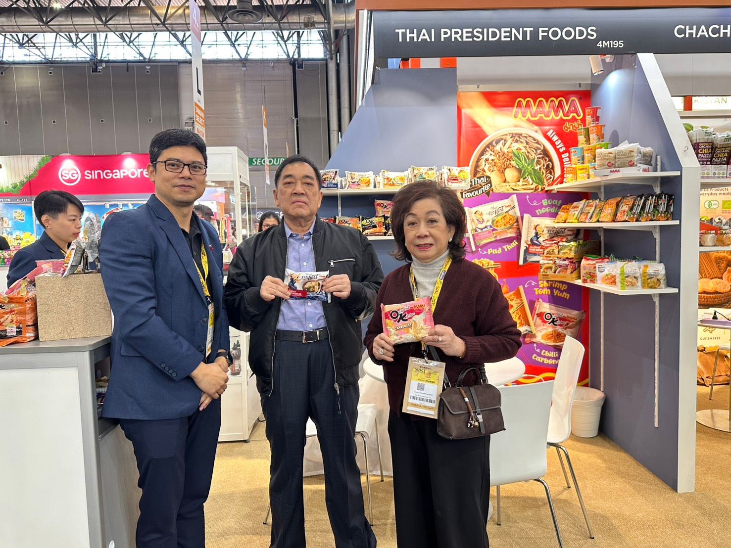 Three people hold Thai President Foods products at a lively trade show booth.