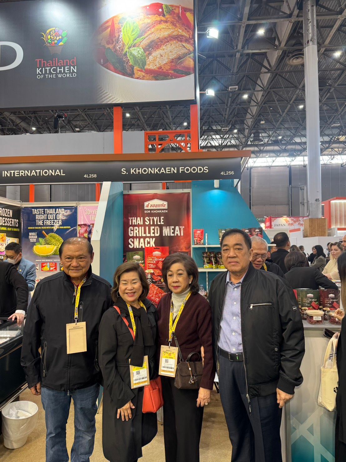 Four professionals smile for a photo at a busy trade show booth.