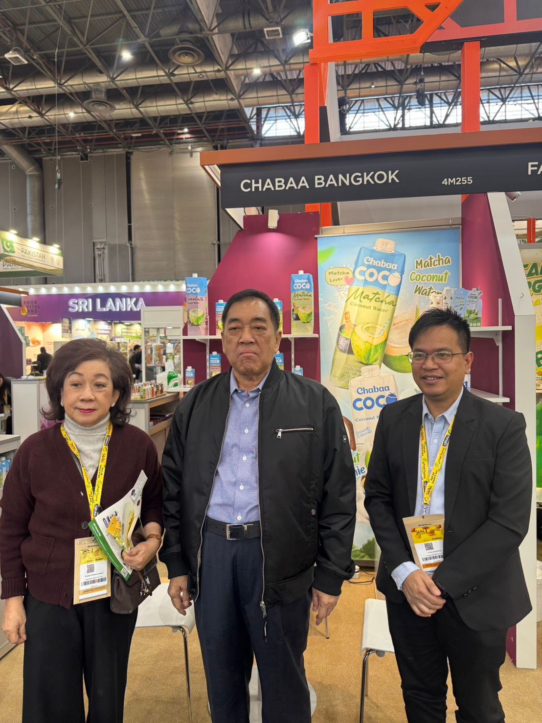 Three people stand at a "Changna Bangkok" trade show booth, likely at an exhibition.