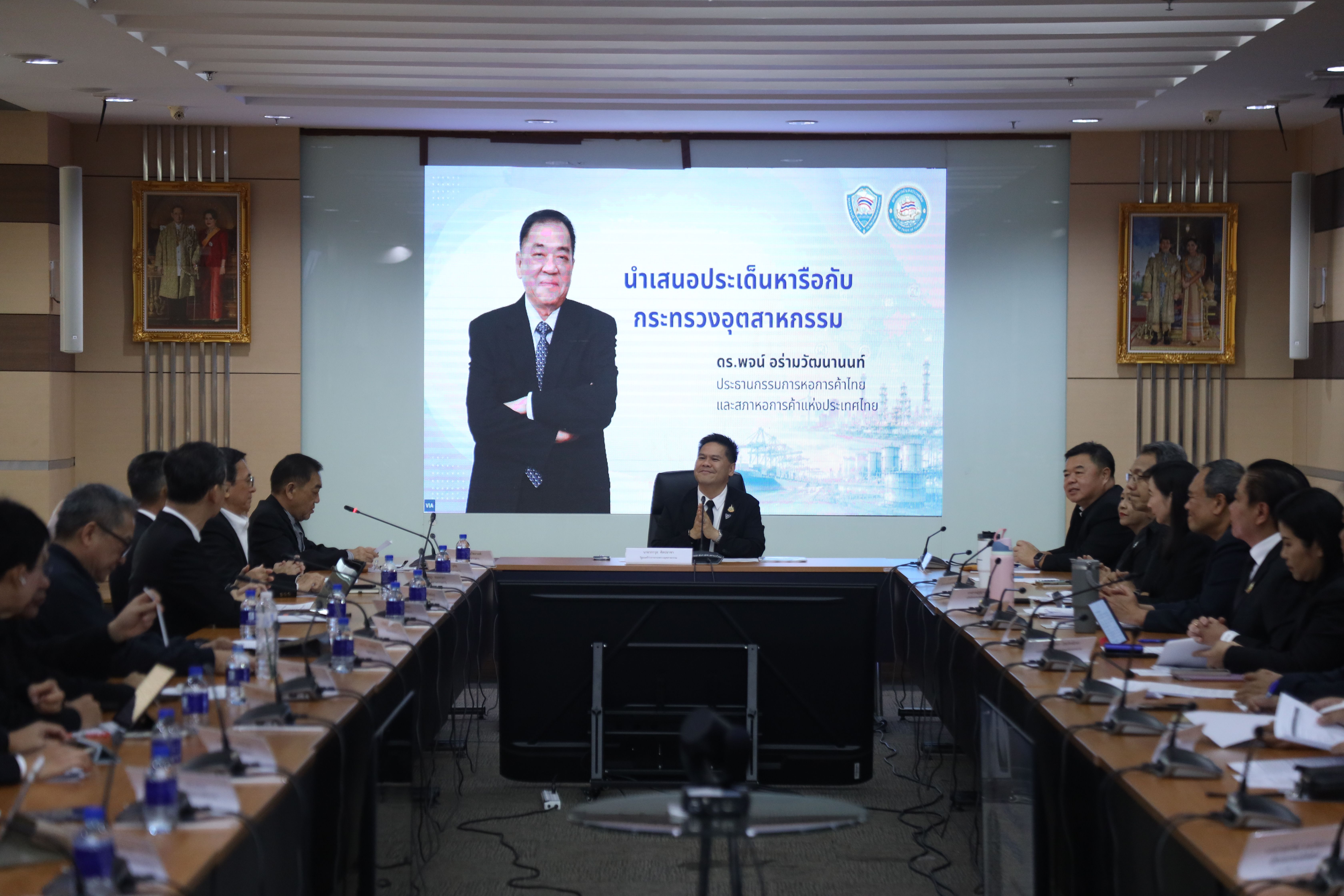 Officials attend a formal meeting around a conference table with a presentation screen.