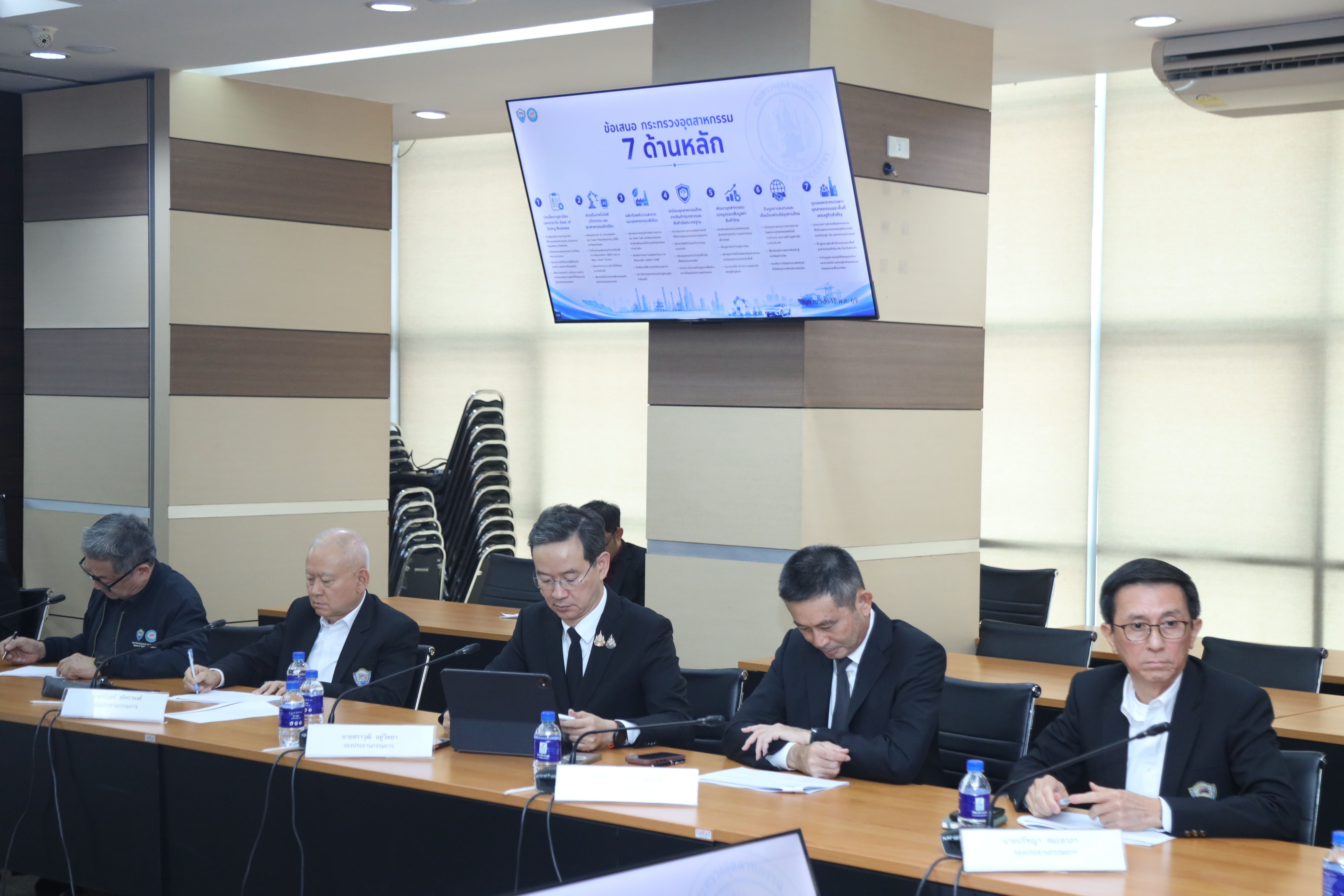 Attendees at a professional meeting table with a presentation screen in the background.