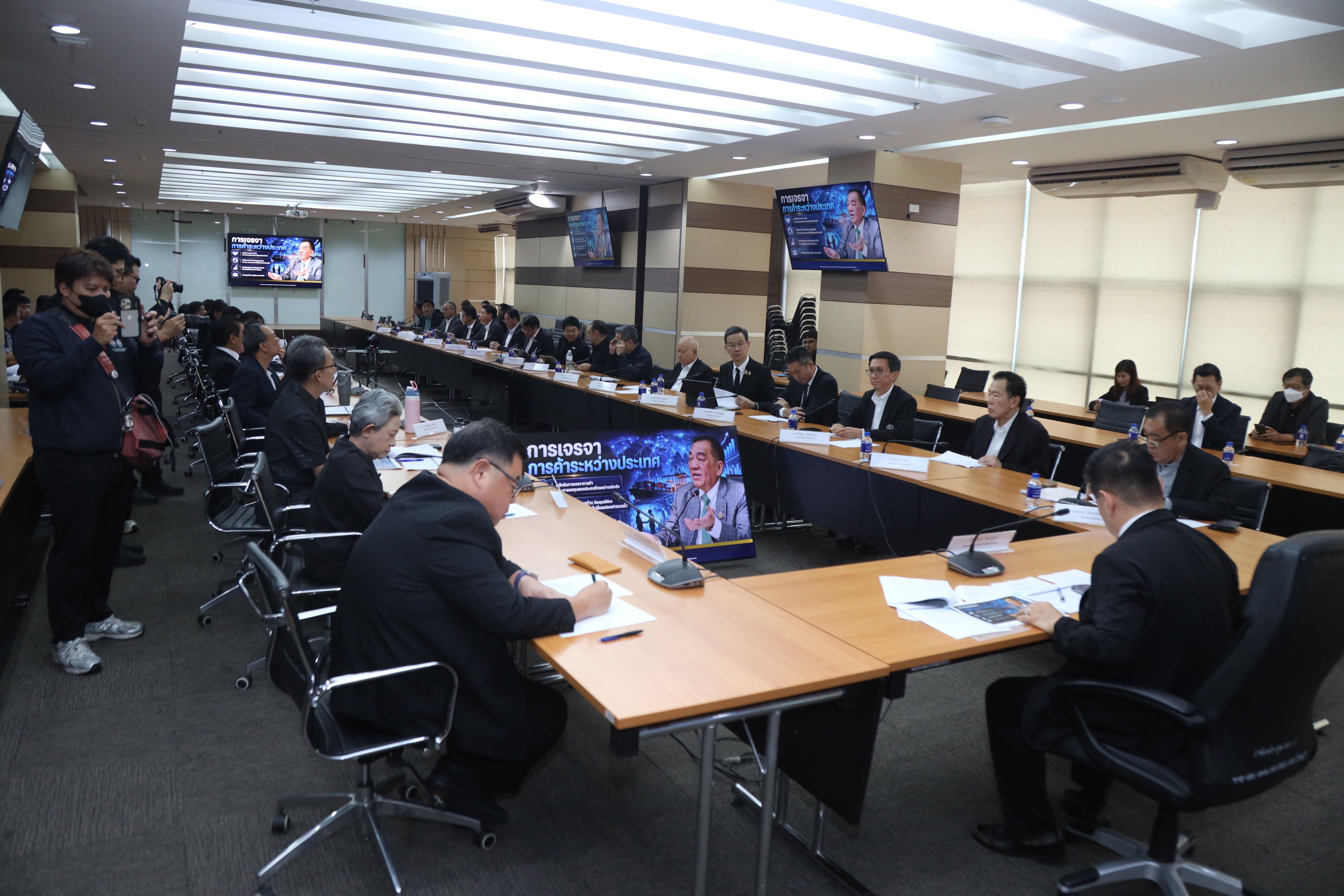 Conference room meeting with professionals, including a video call participant on a central screen.