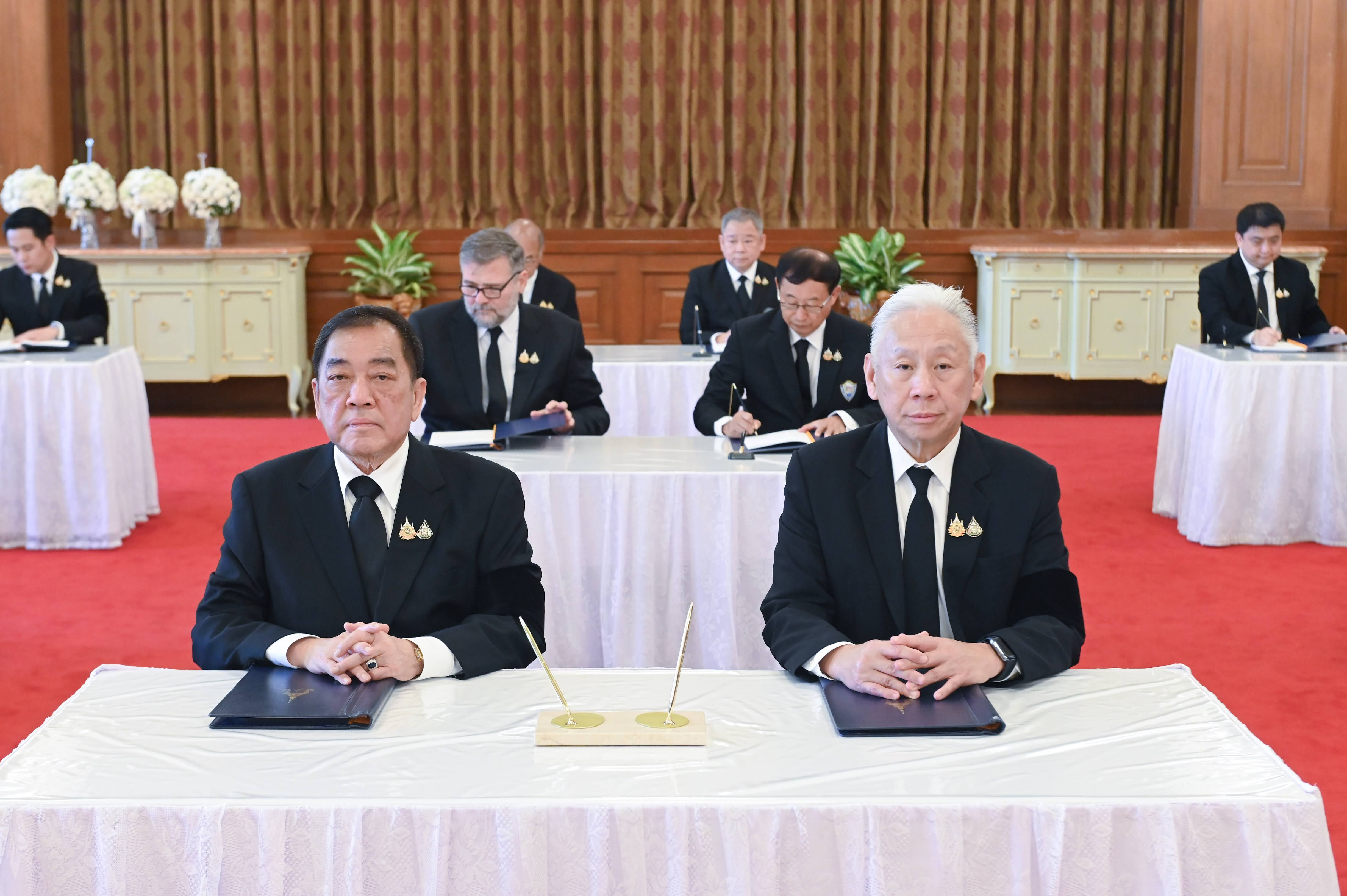 Two men in formal black suits with medals seated at a table during a signing ceremony.