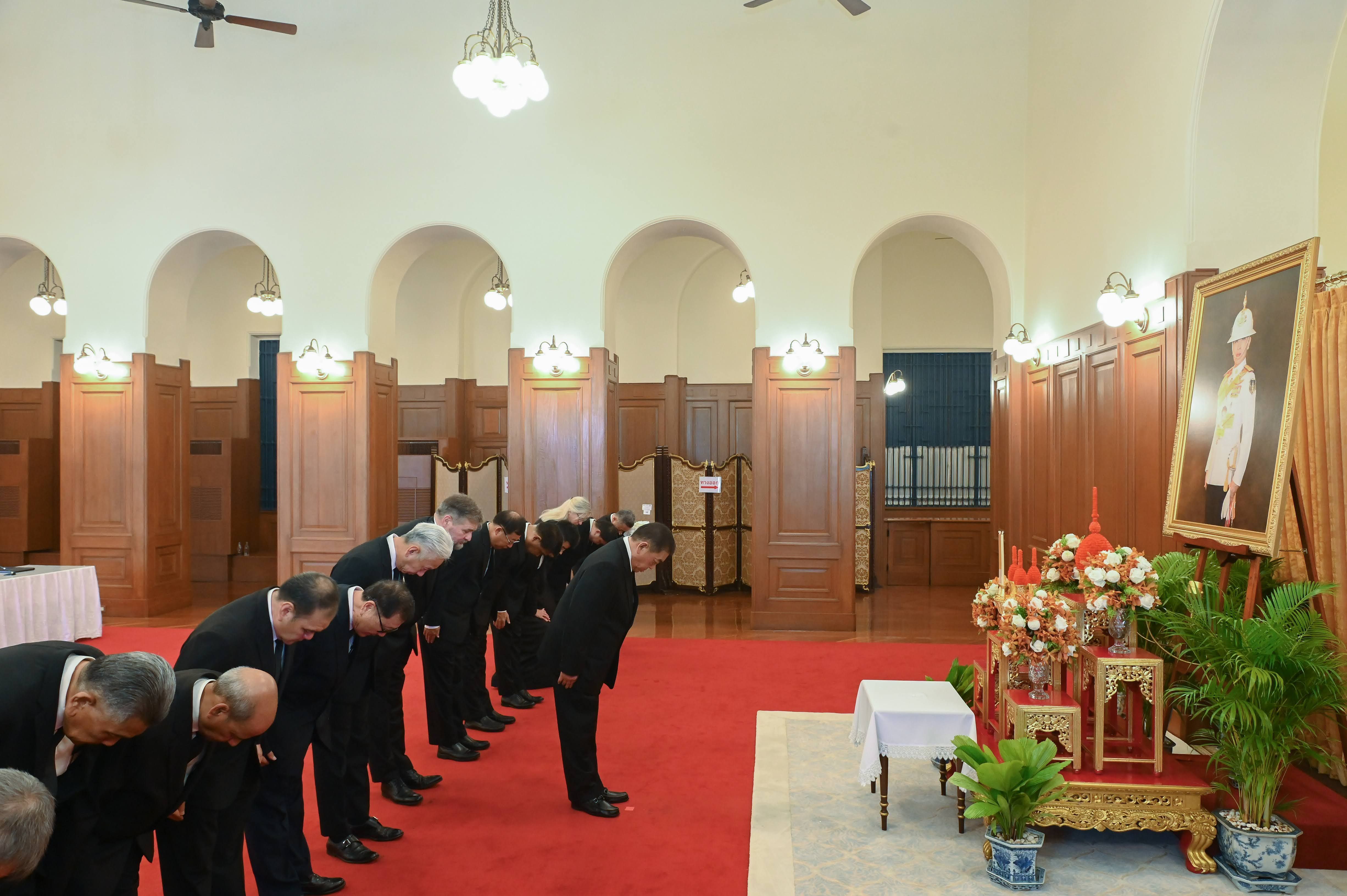 Men in suits bow before a framed portrait and ornate altar in a formal room.