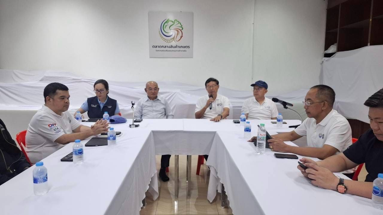 Men sit around a white table in a meeting room, one speaks into a microphone.