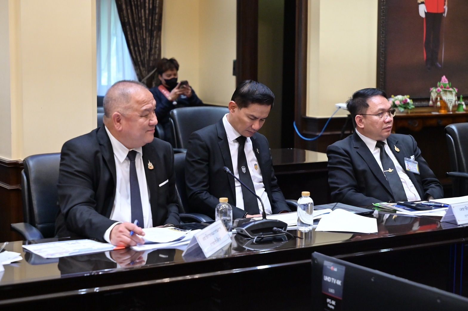 Three men in black suits attending a formal meeting at a large conference table.