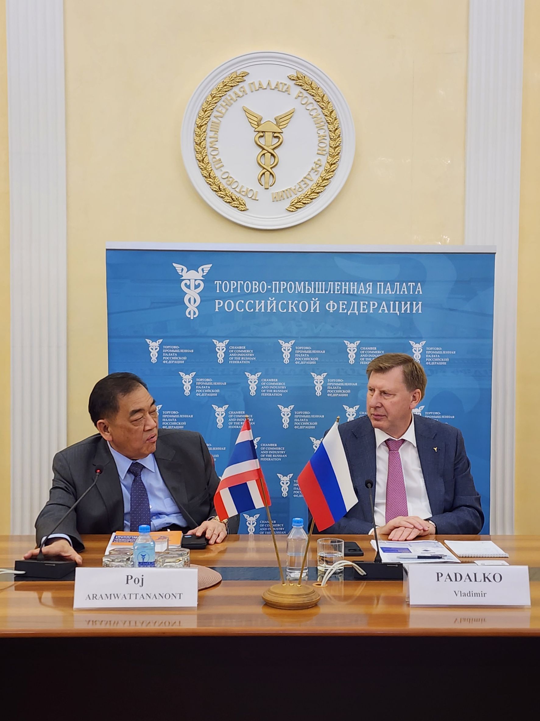 Two diplomats, Thai and Russian, sit at a table with flags during a formal meeting.