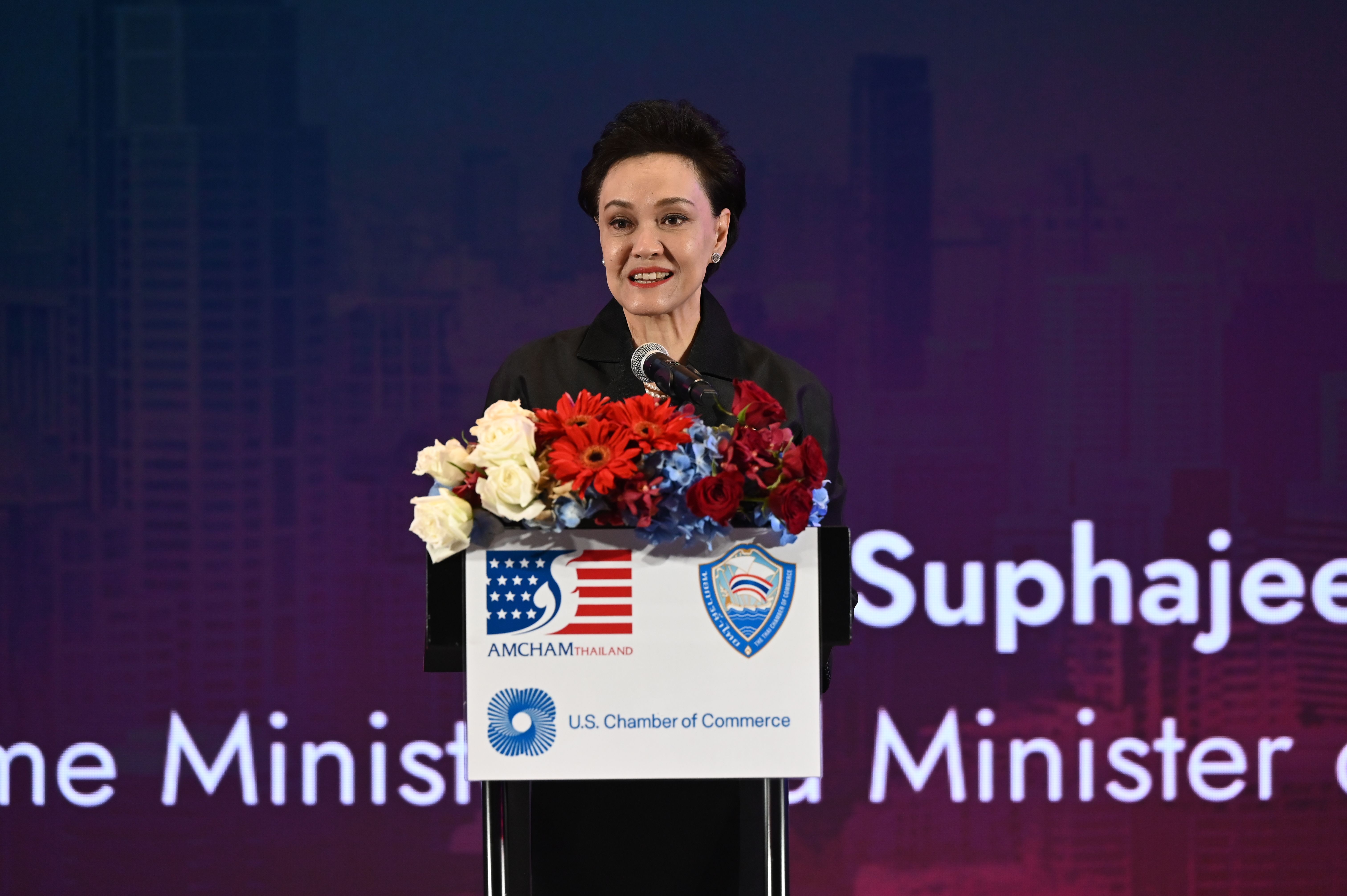 Woman speaks at a podium decorated with flowers and American Chamber of Commerce logos.