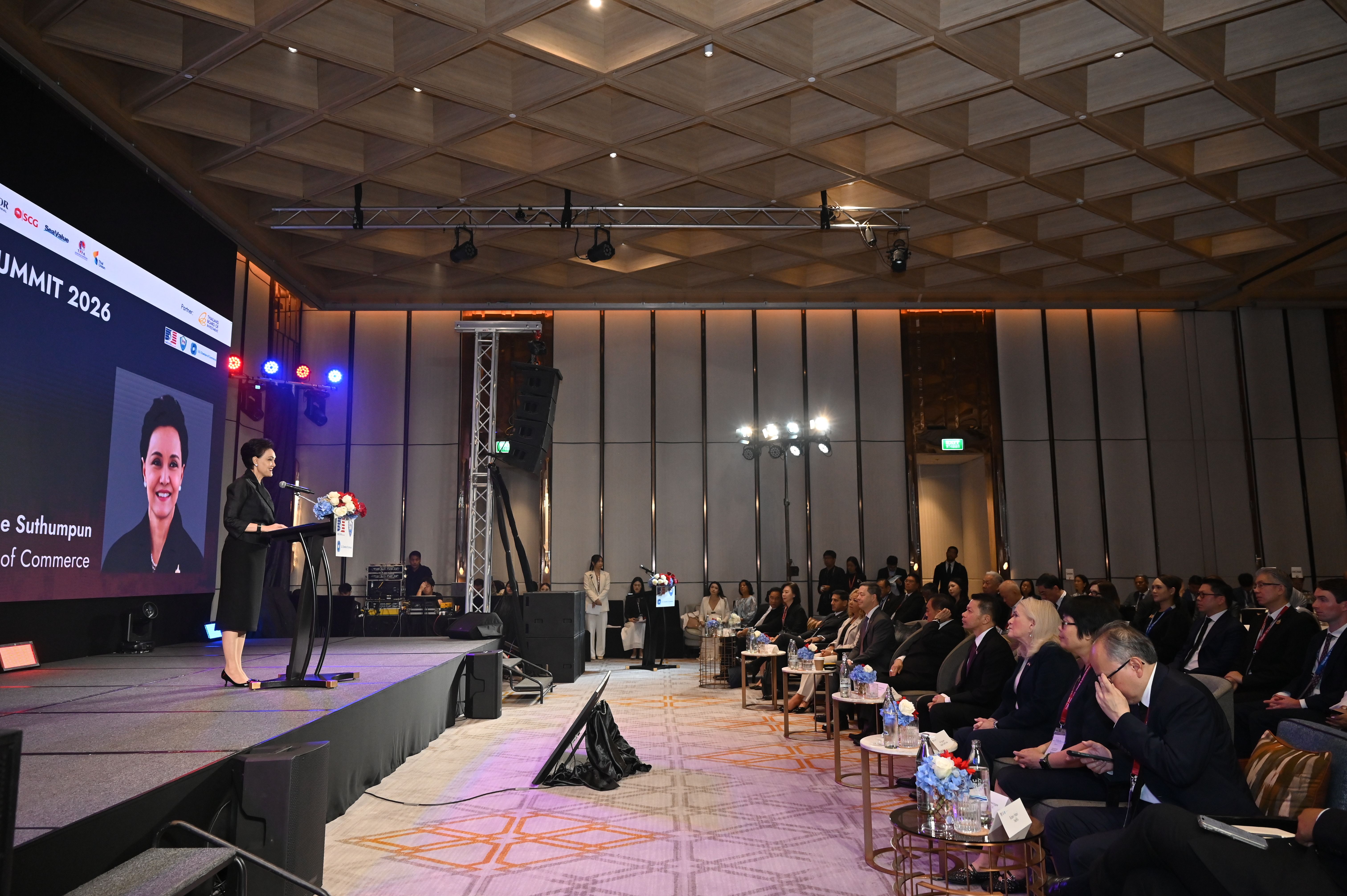 Woman presents at a conference, speaking from a podium with her image on a large screen.