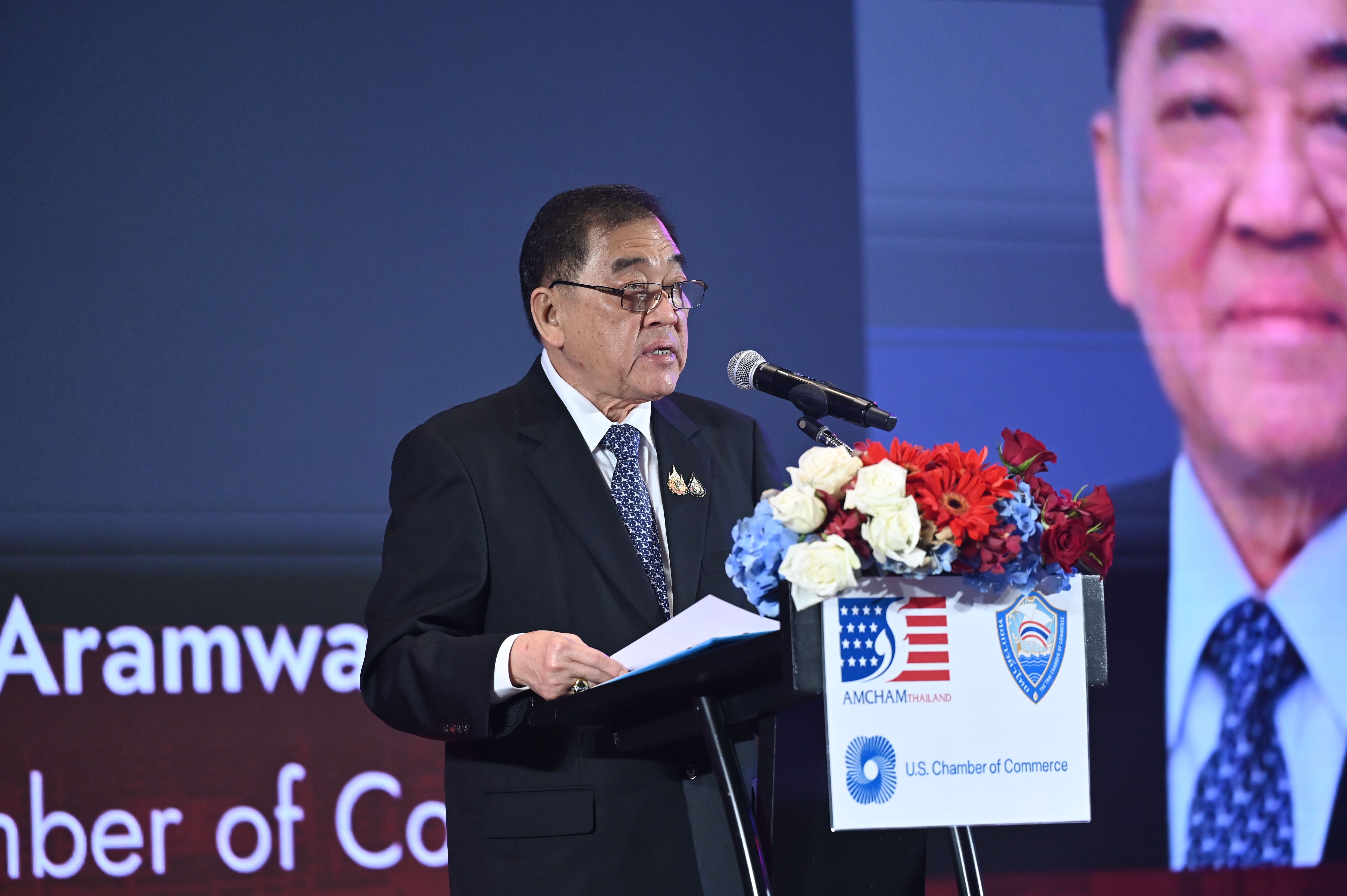 Man in a dark suit speaks at a podium with a microphone at a formal event.