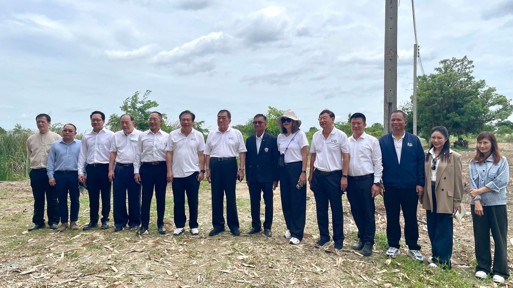 Group of professionals in business casual attire standing outdoors in an undeveloped area.
