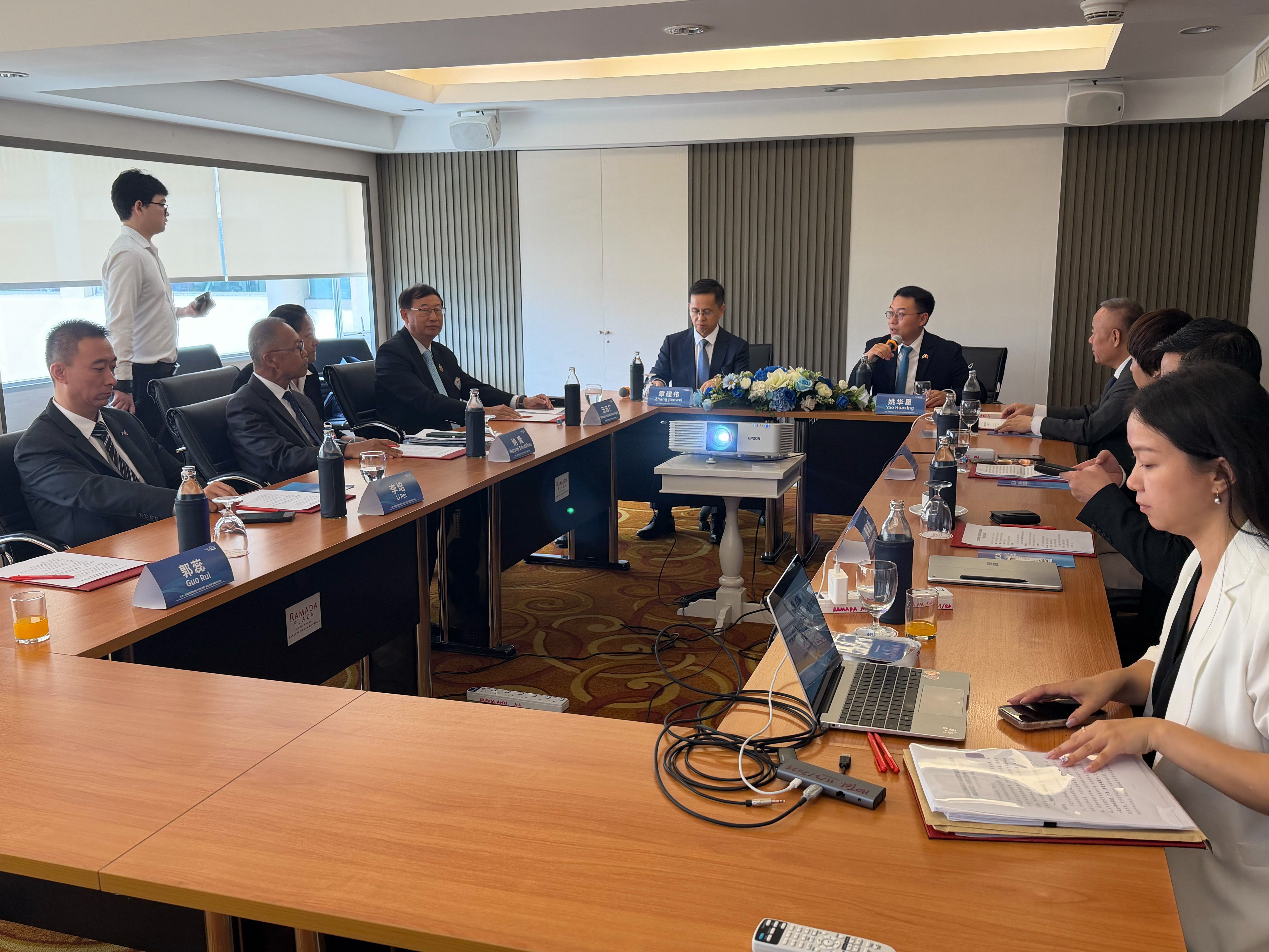 Business meeting with several professionals seated around a U-shaped table, one person presenting.