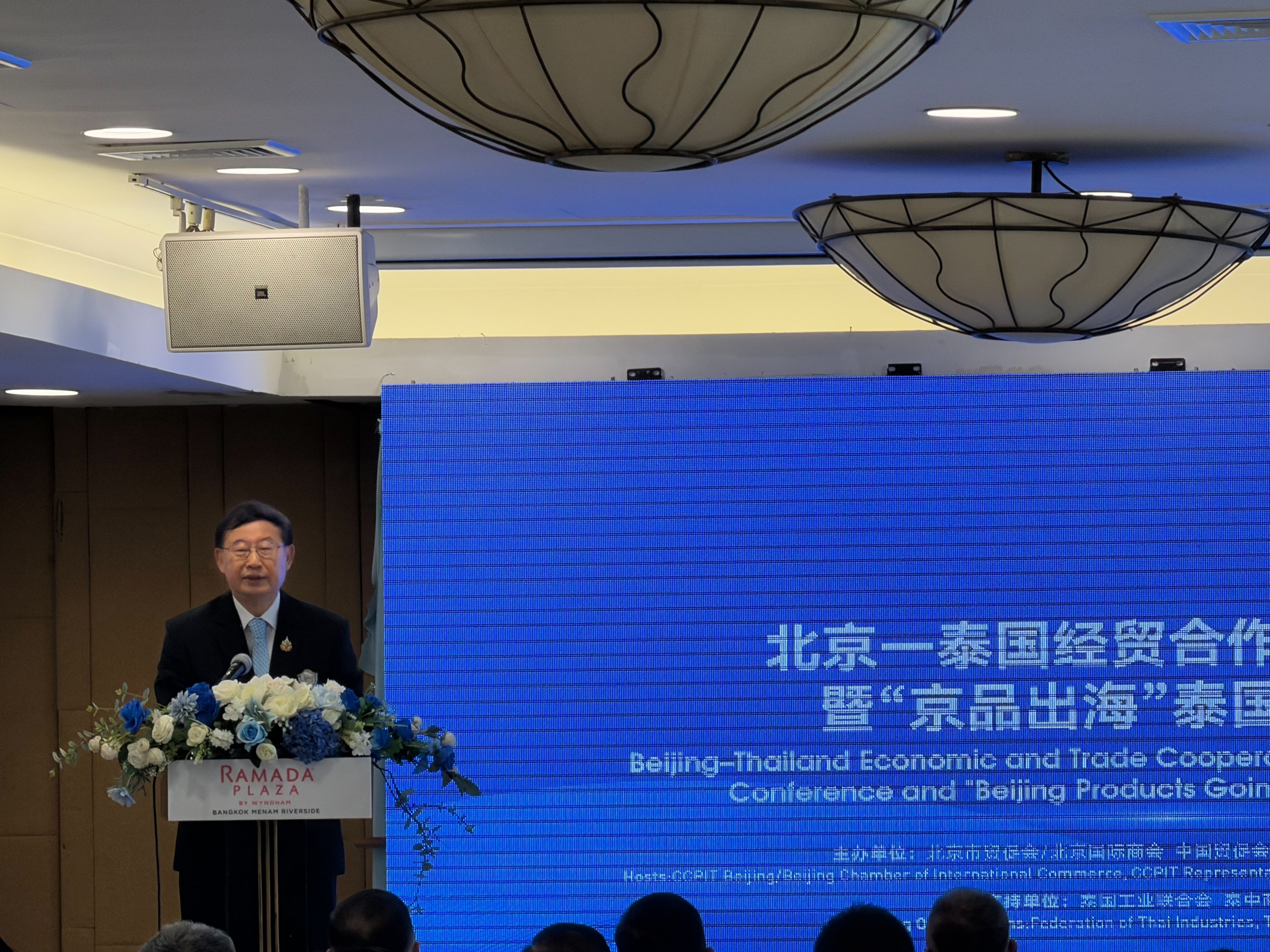 Man speaks at podium during Beijing-Thailand Economic and Trade Cooperation conference.