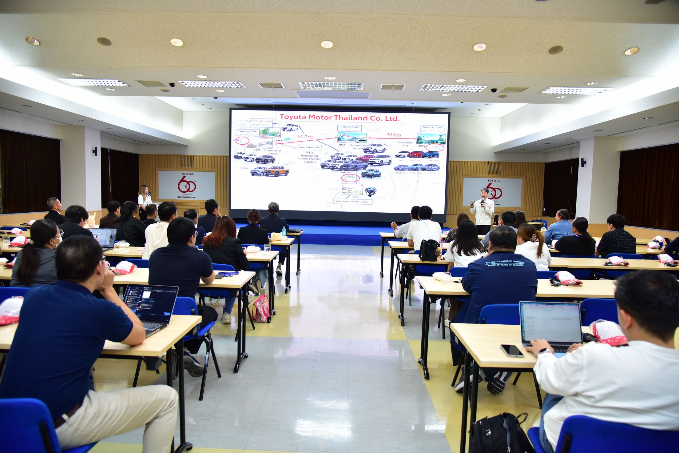 Attendees observe a complex diagram on a large screen in a modern conference room.