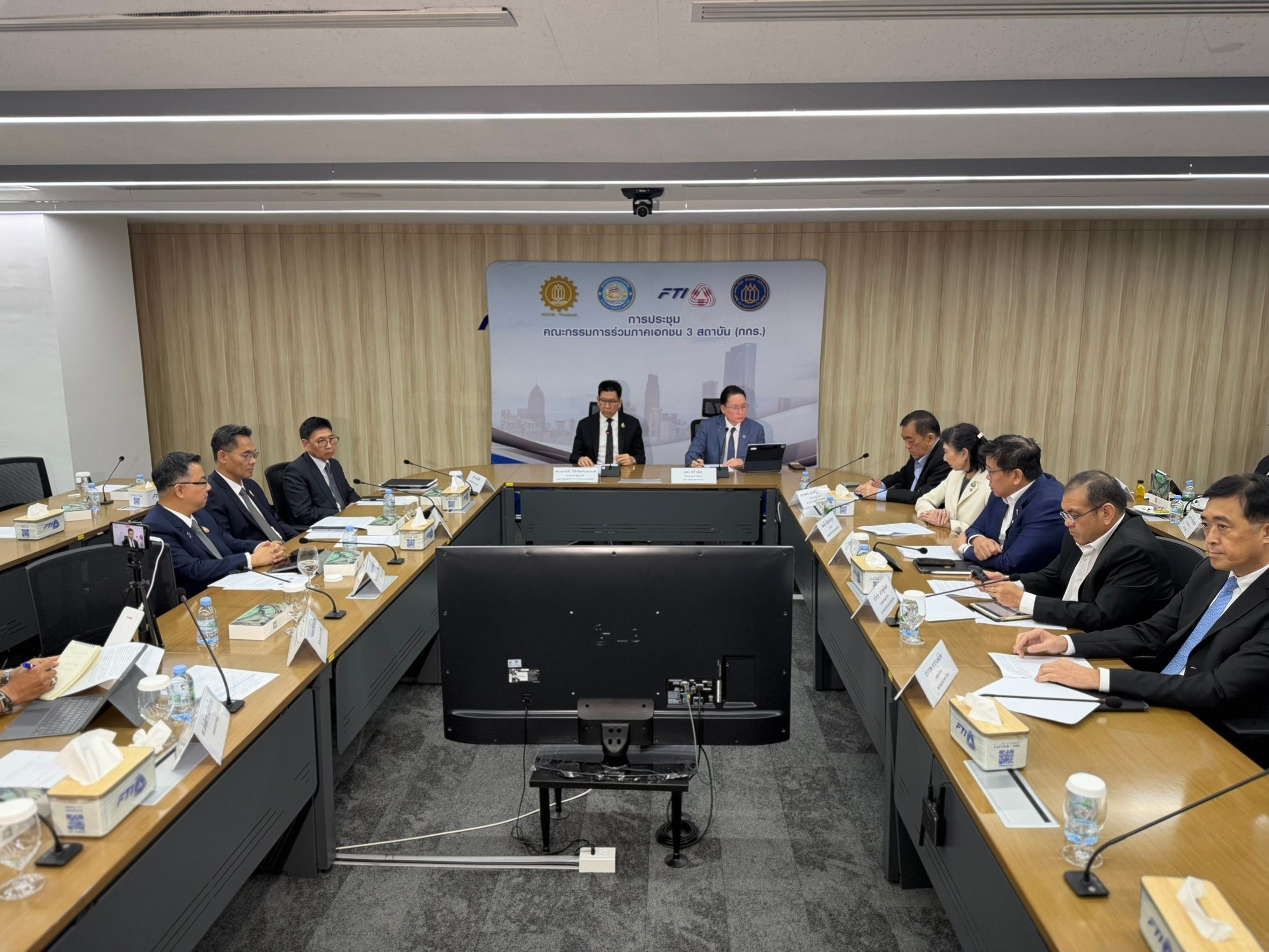 Professionals attend a formal meeting around a conference table with a presentation screen.