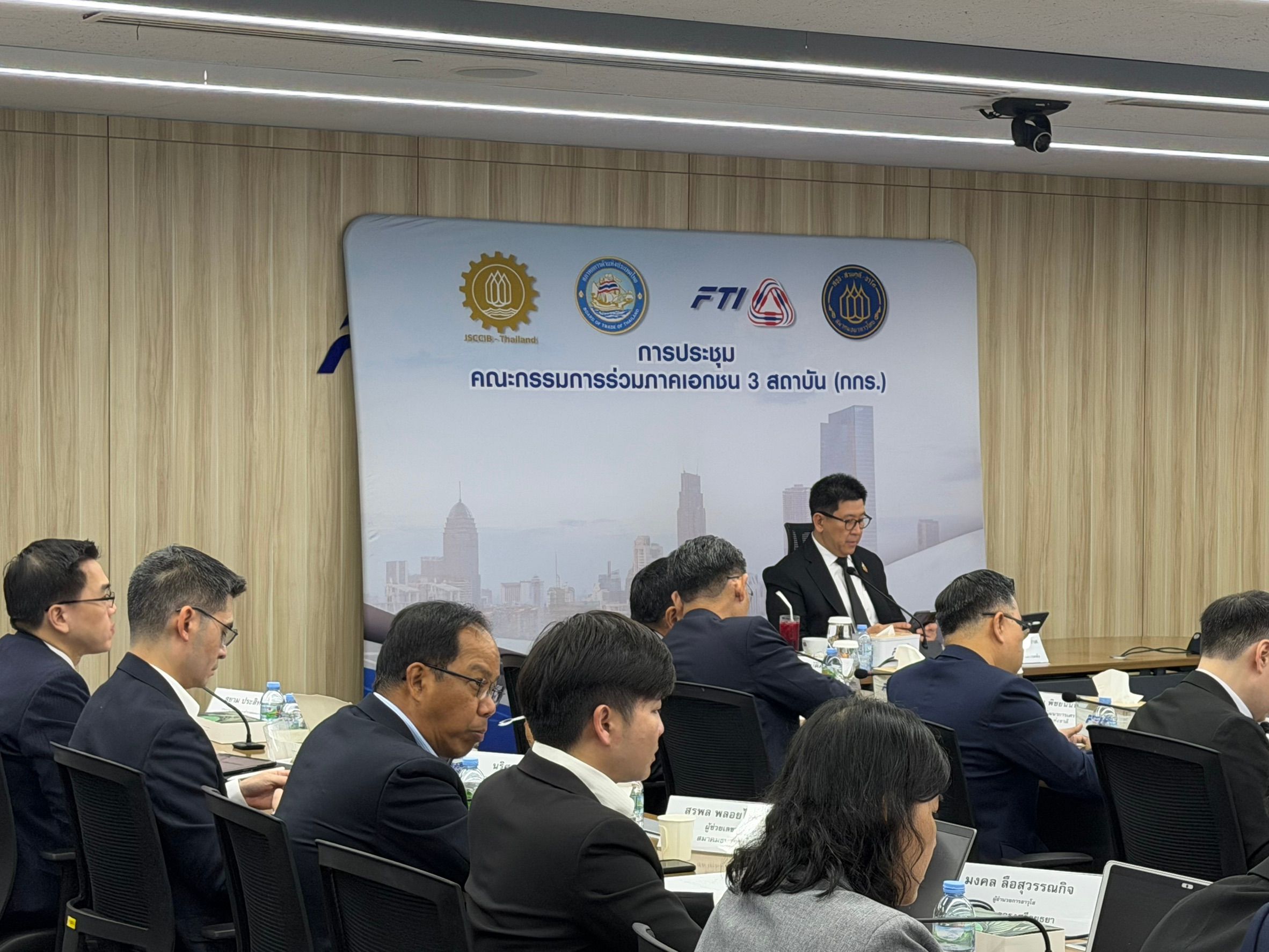 Professionals in suits attend a formal business meeting at a long conference table.
