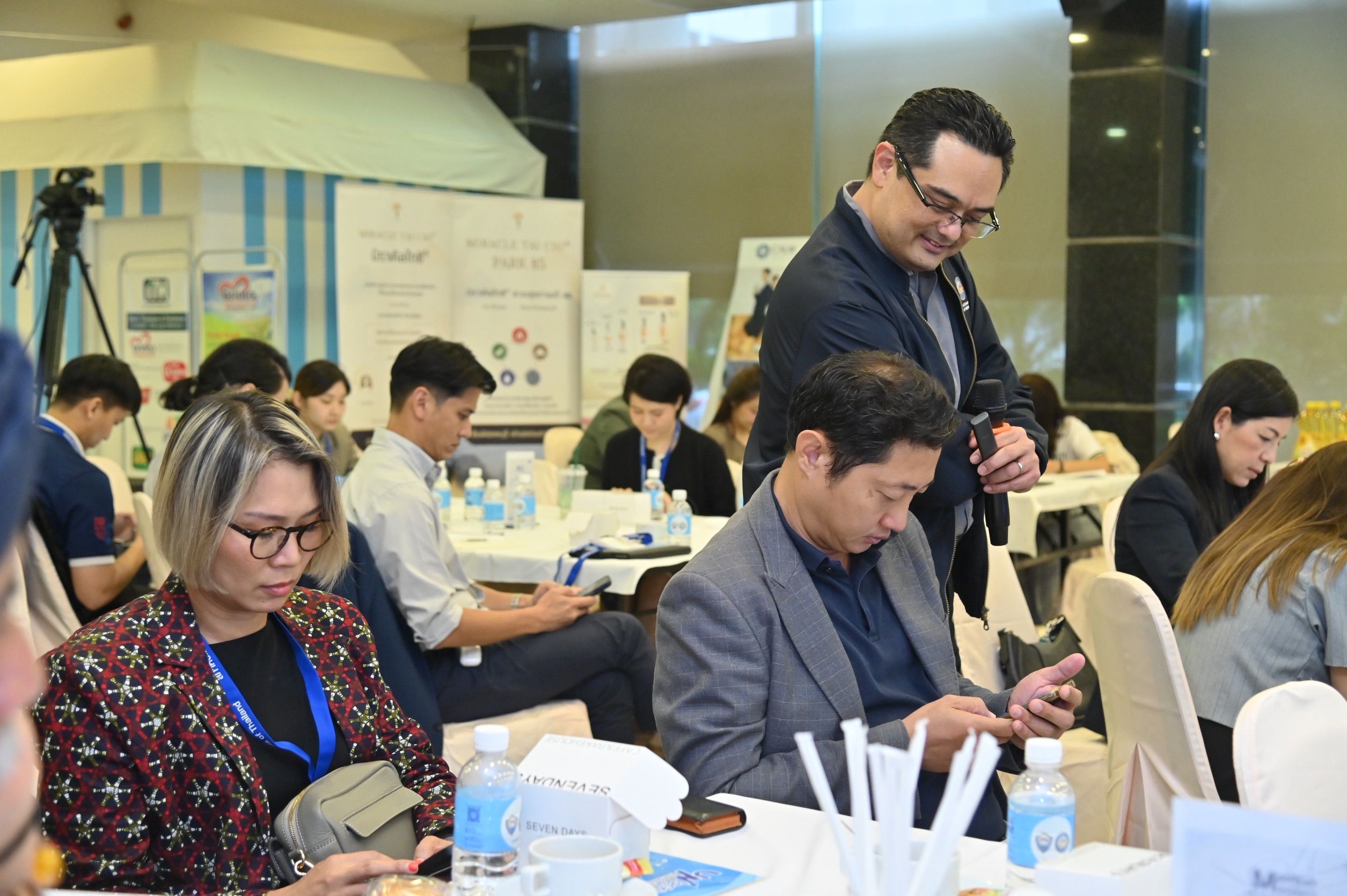A man in a blue shirt stands over seated workshop attendees engaged with their devices.