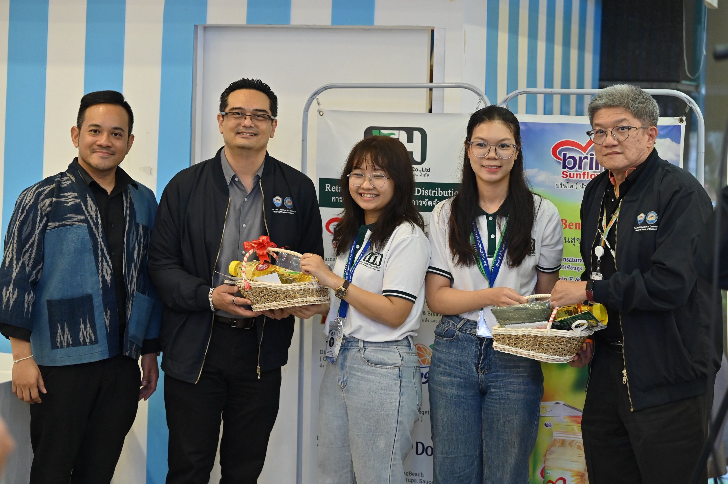 Five smiling people, two women receiving fruit baskets from three men at an event.