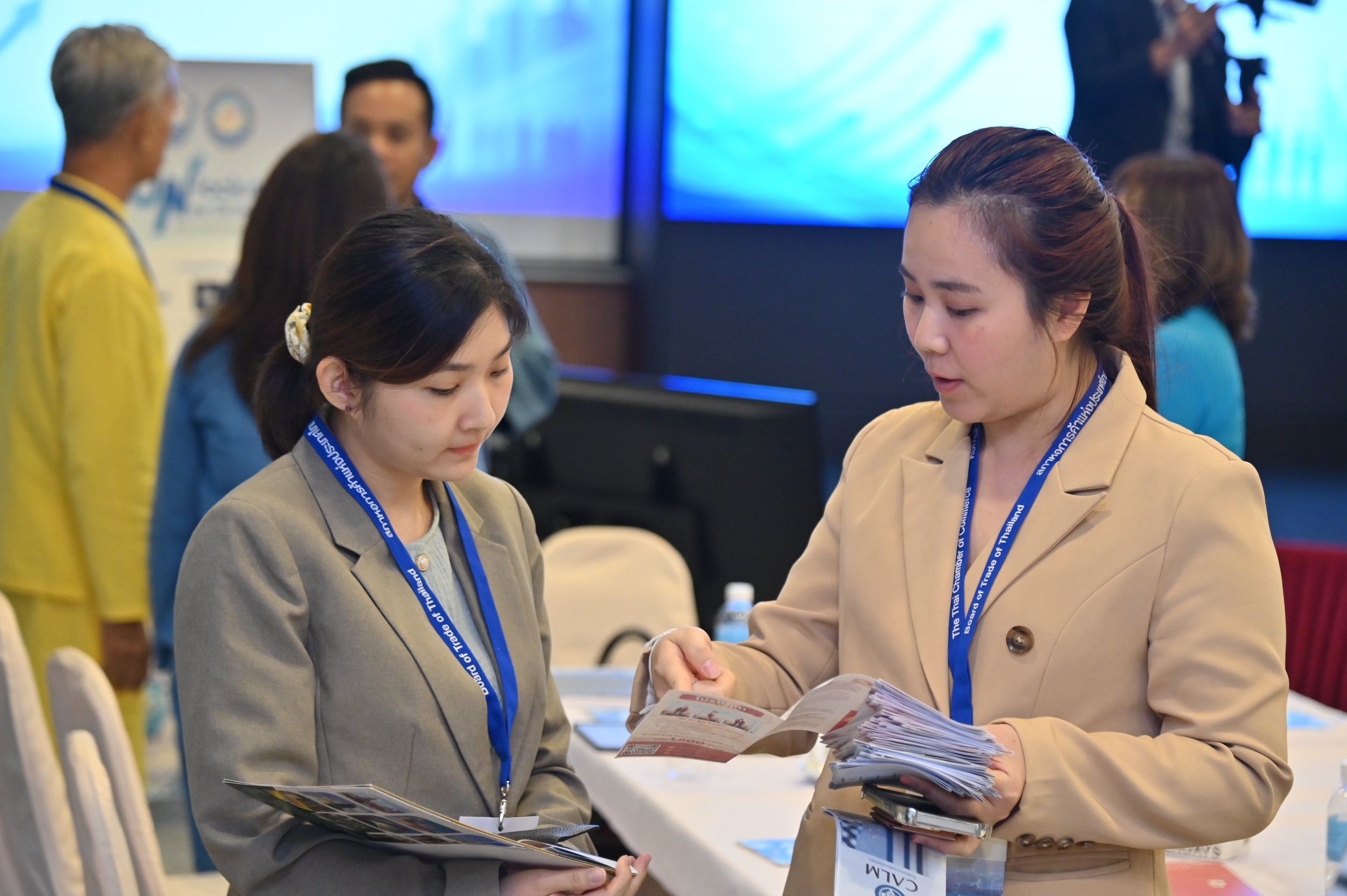 Two professional women discuss brochures at a conference or networking event.