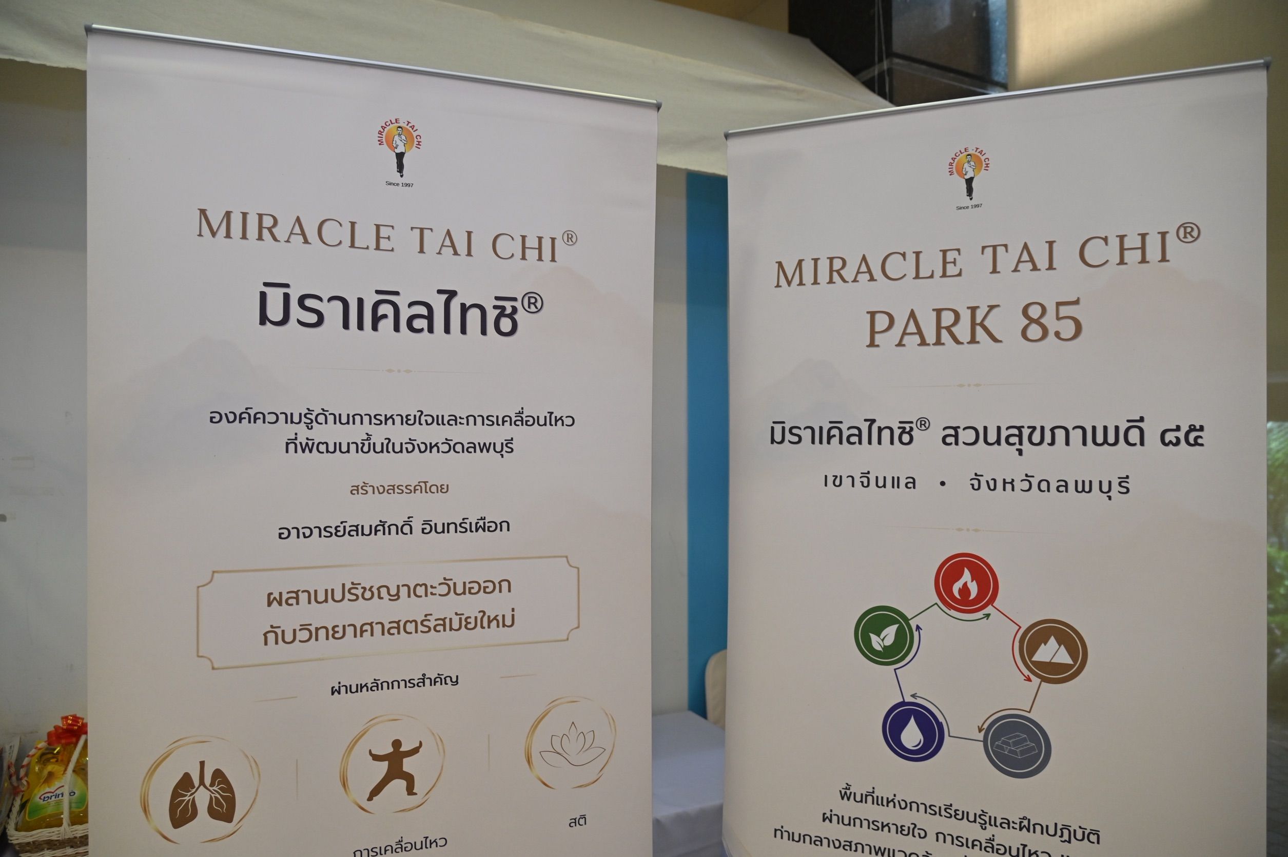 Two white promotional banners advertise 'Miracle Tai Chi' and 'Park 85' with Thai text and icons.