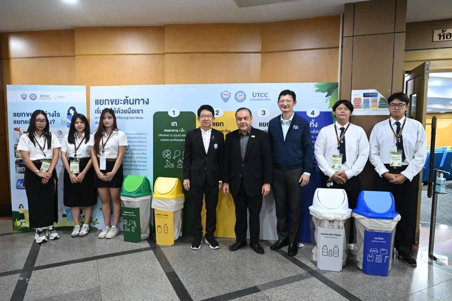 Group of students and adults posing with colorful recycling bins at an event.