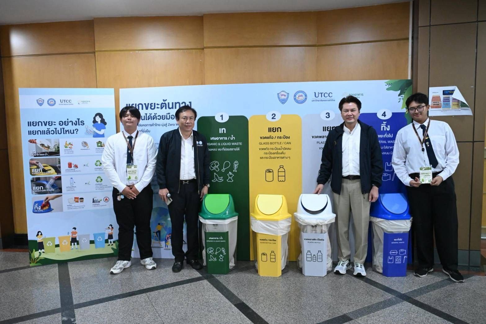 Four men stand beside diverse recycling bins and informational waste sorting posters.