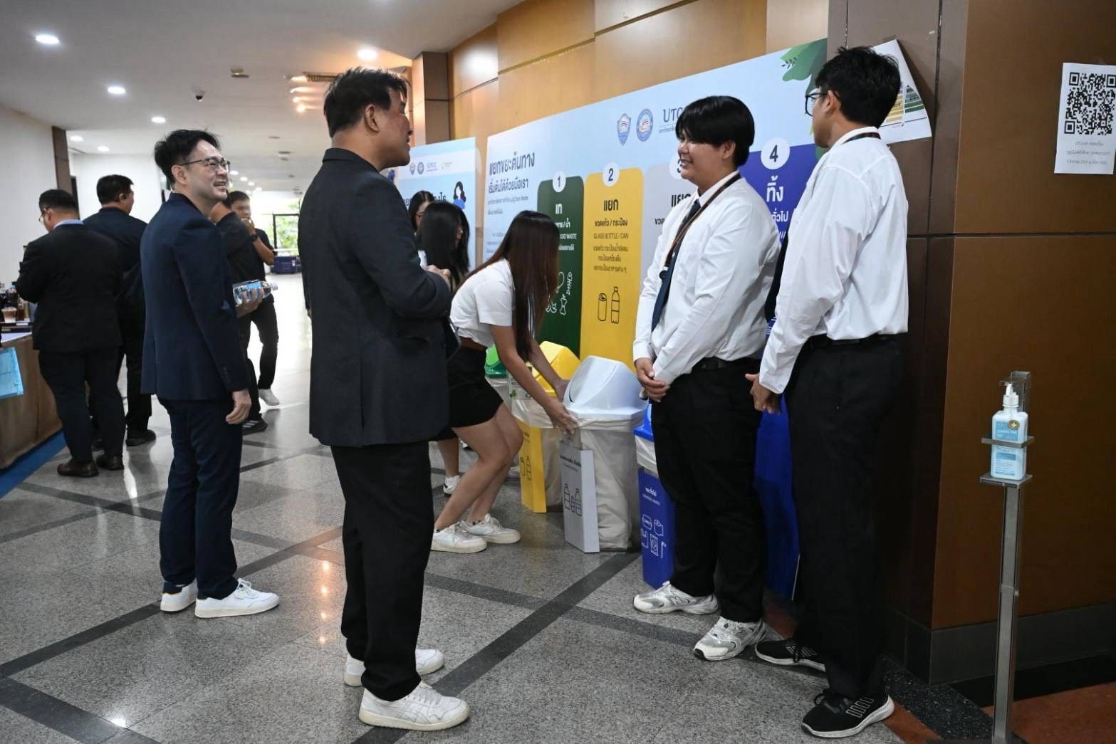 People in a modern hallway discussing proper waste segregation techniques near colorful recycling bins.
