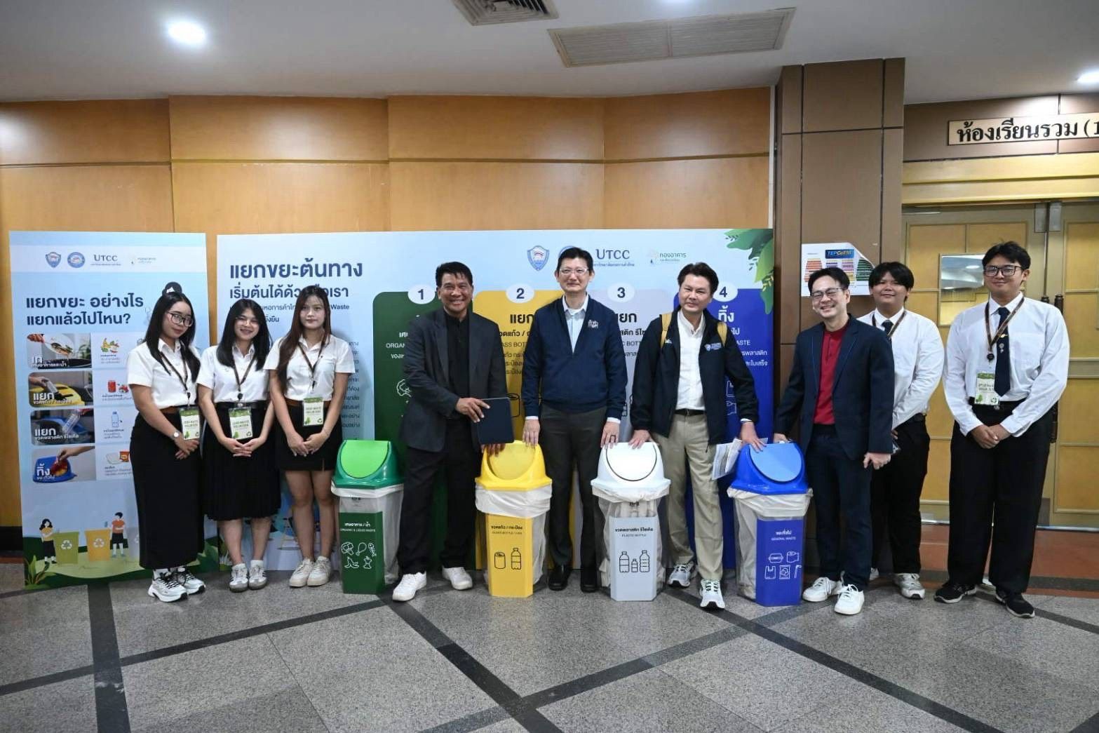 Diverse group of people standing with various recycling bins in front of informational displays.
