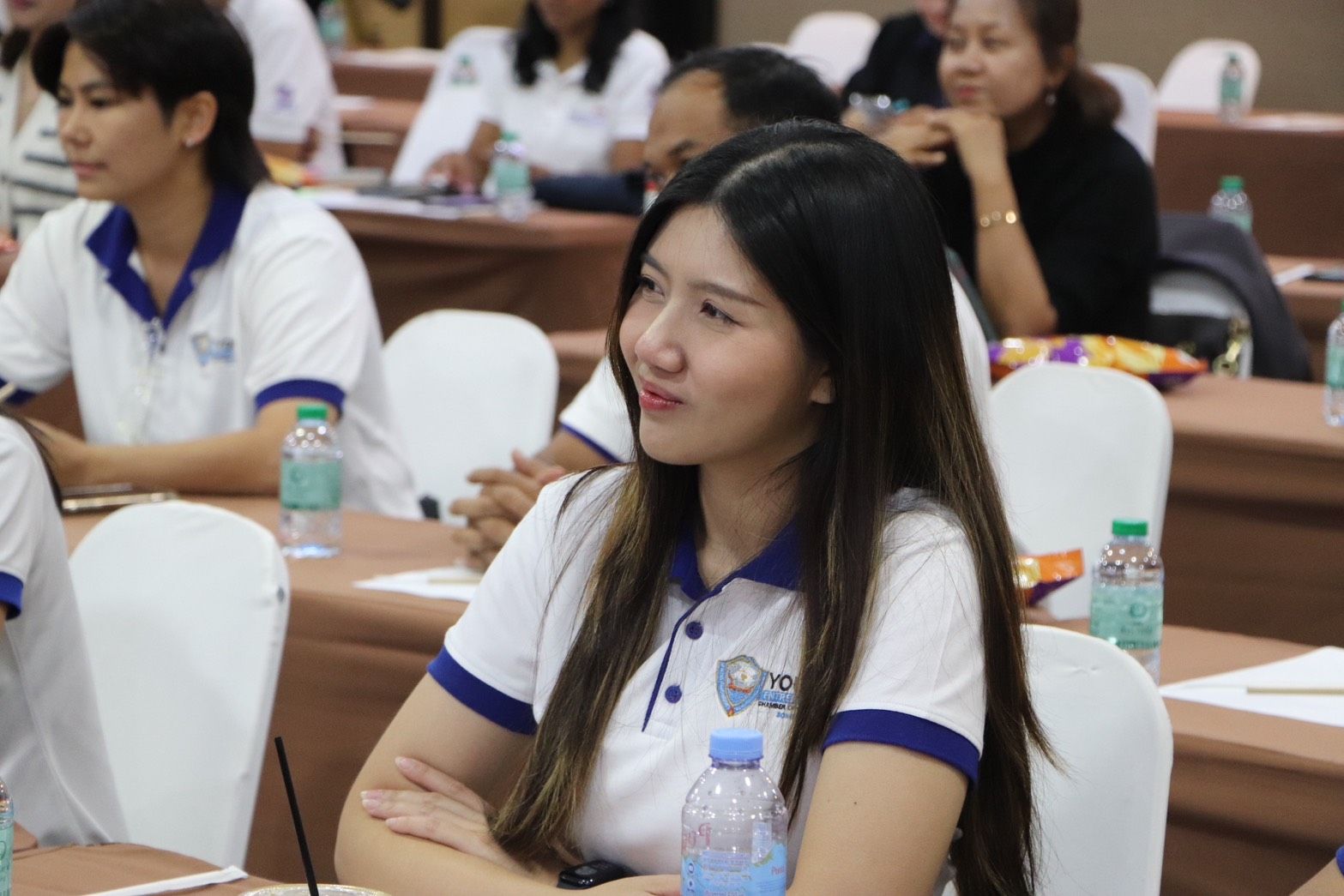 Smiling young woman with long hair listening attentively in a conference room.