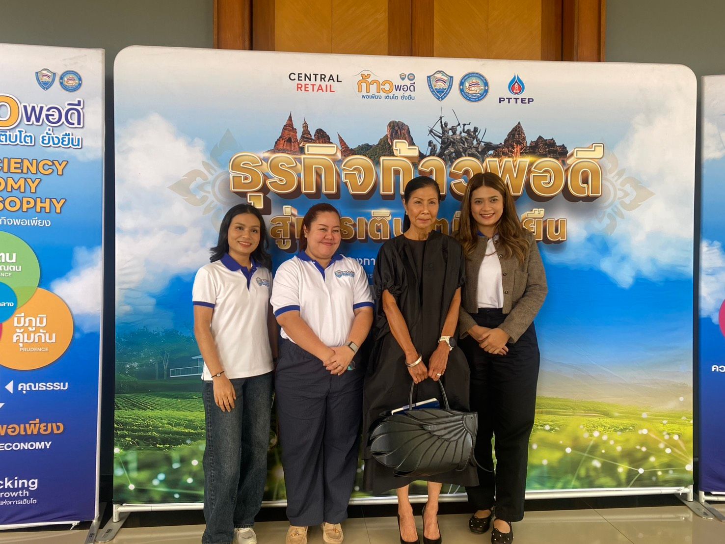 Four women posing together in front of a branded blue and white backdrop.