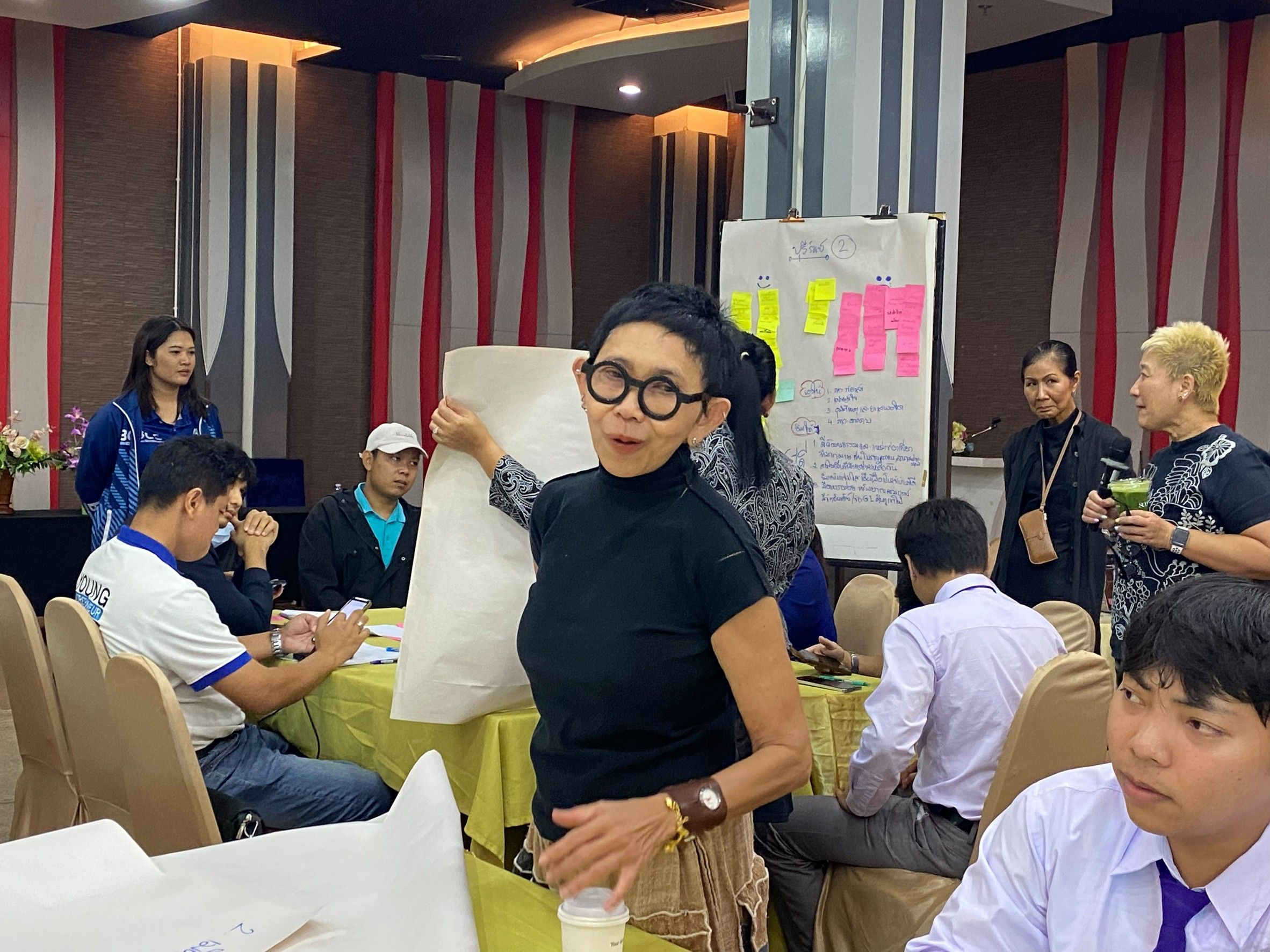 Woman in glasses presenting to a group of people during a workshop.