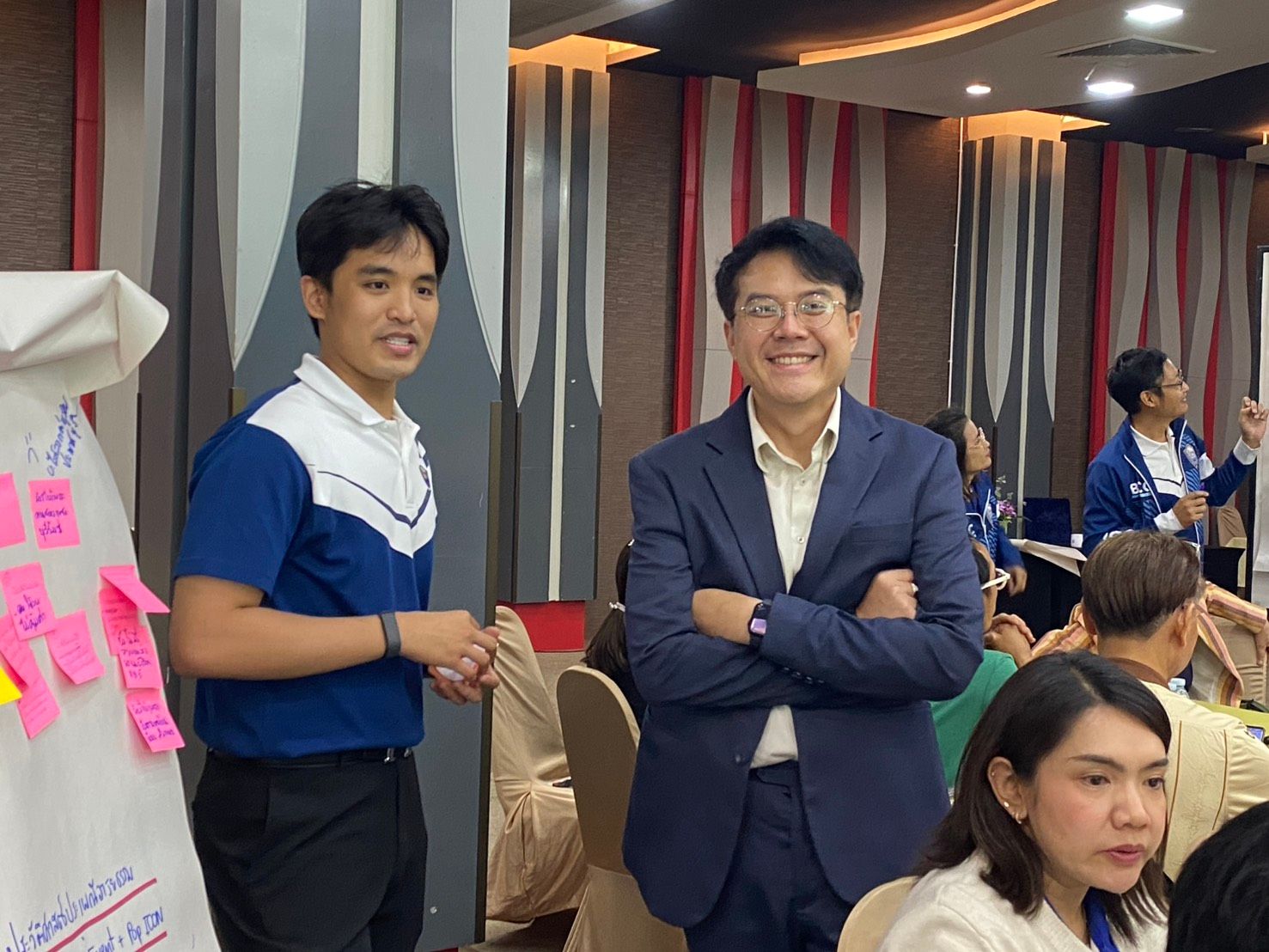 Smiling man in a suit and a younger man in a polo stand at a workshop.