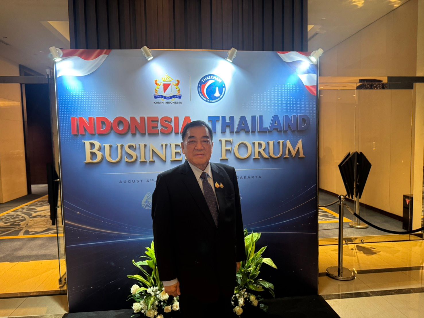 A man in a dark suit stands before an 'Indonesia Thailand Business Forum' banner.
