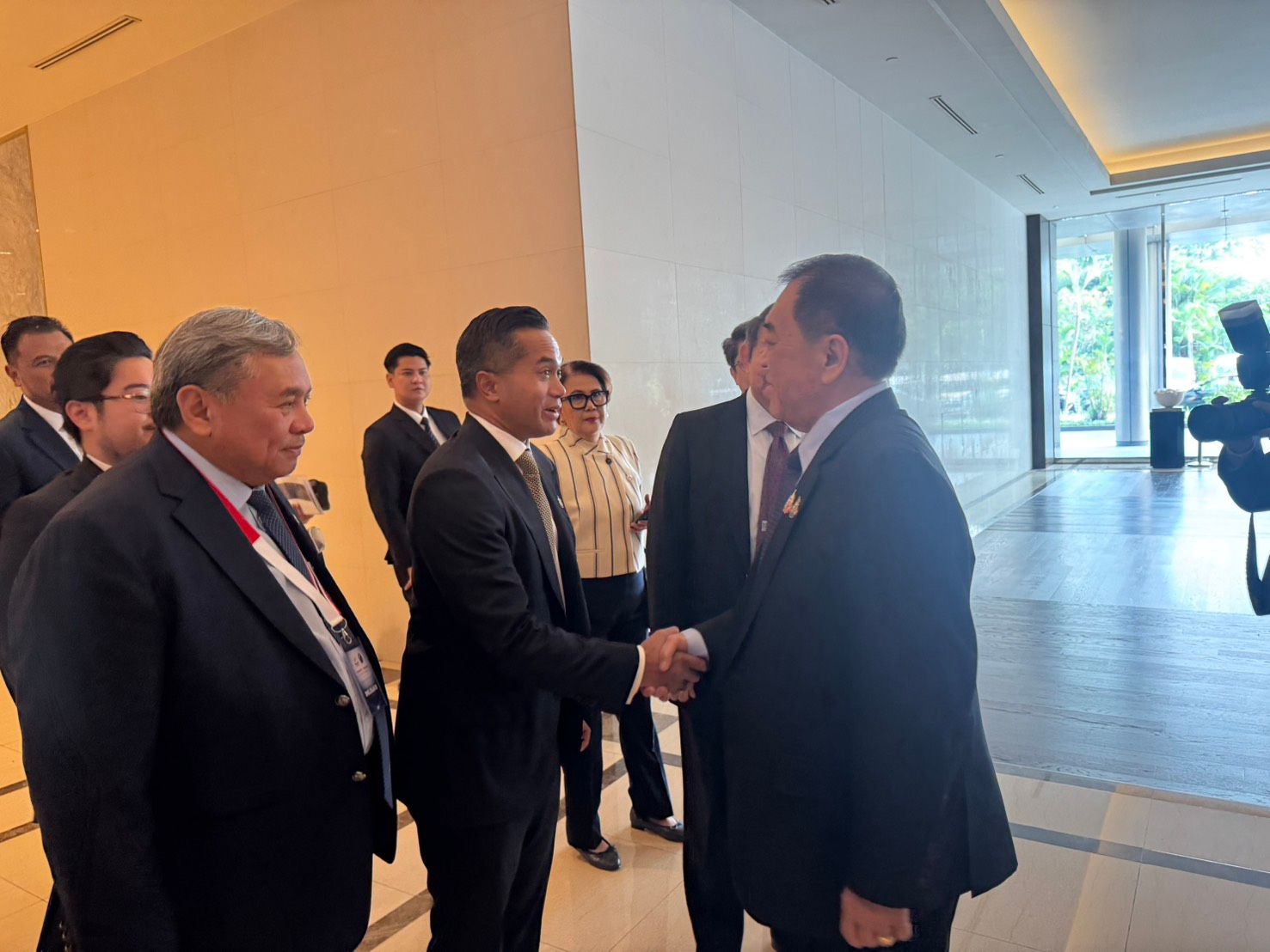 Two men in dark suits shake hands, signaling a formal greeting inside a modern building.